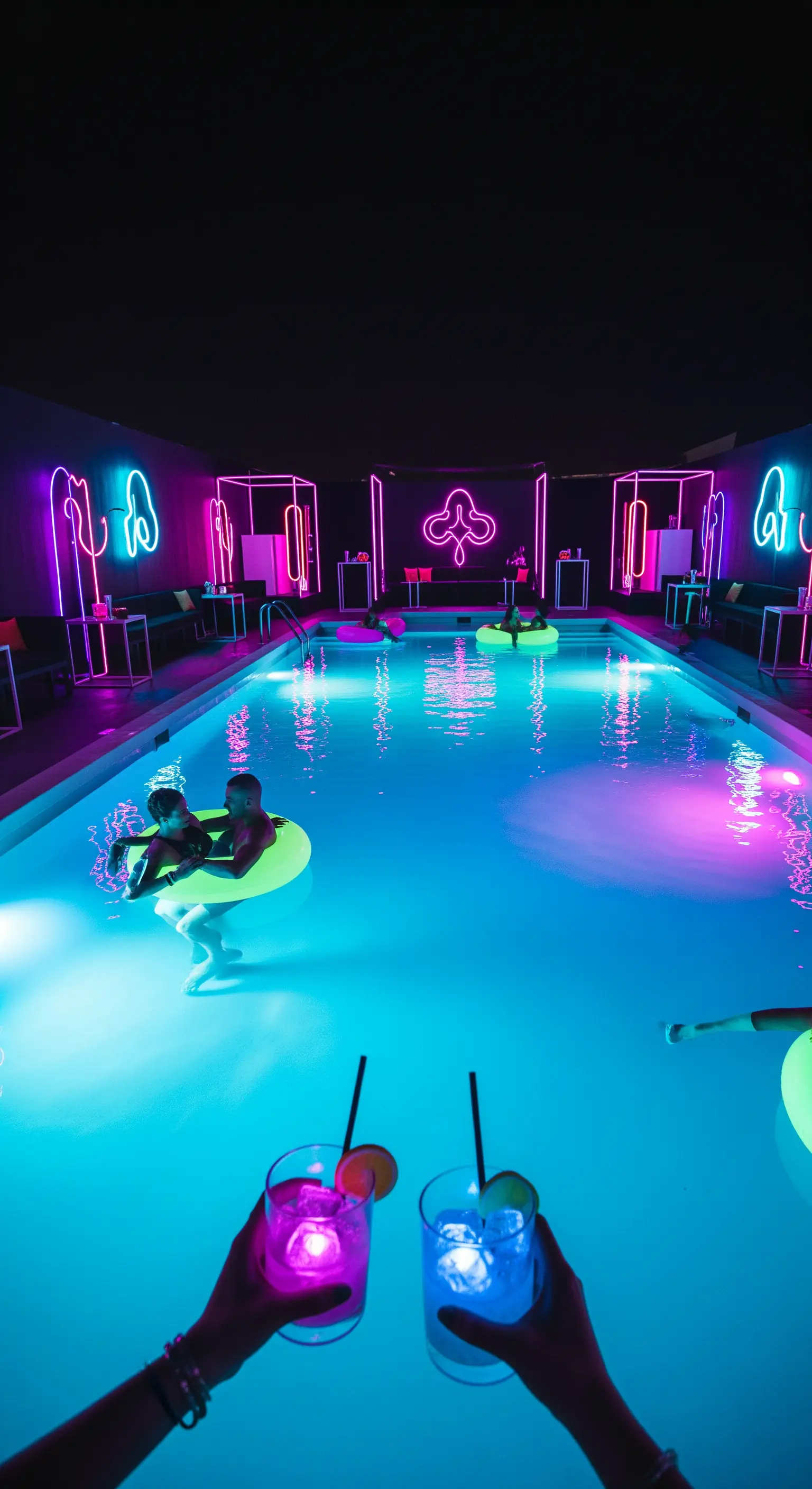 Pool party indoor con luci al neon blu e viola che si riflettono sull'acqua.