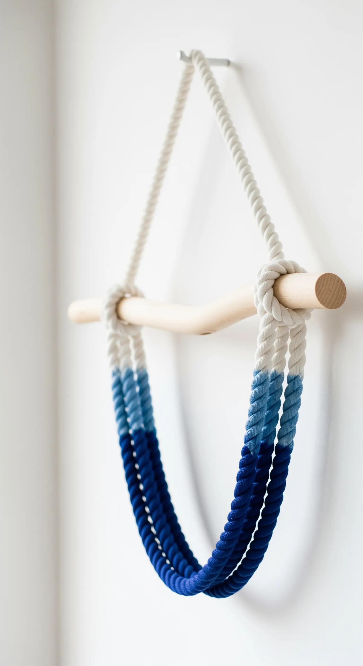 Bastone di legno chiaro con corde di cotone spesse tinte a gradiente nelle tonalità del blu.