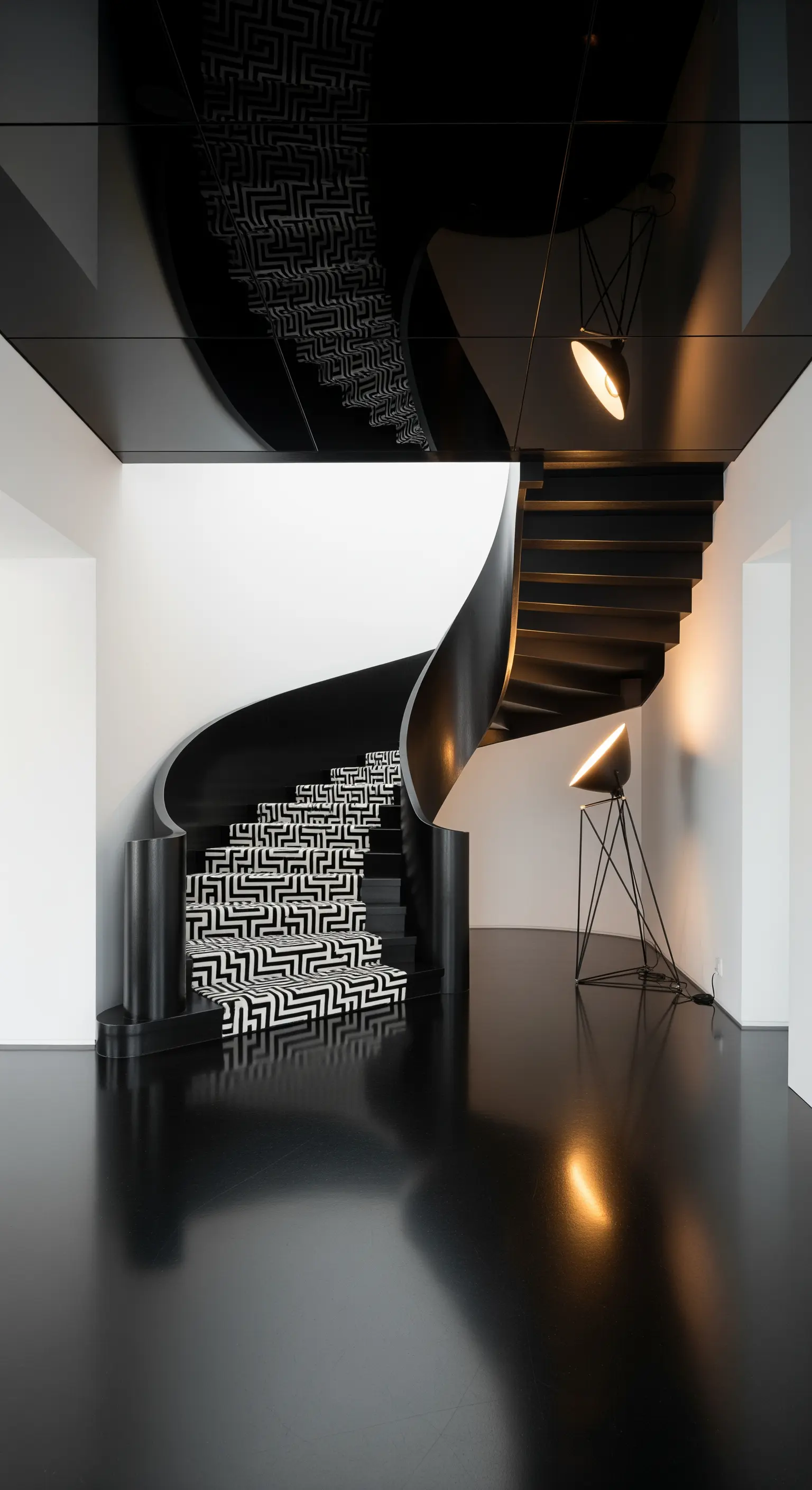 Scala a chiocciola nera con un runner a motivo geometrico bianco e nero, illuminata da faretti.