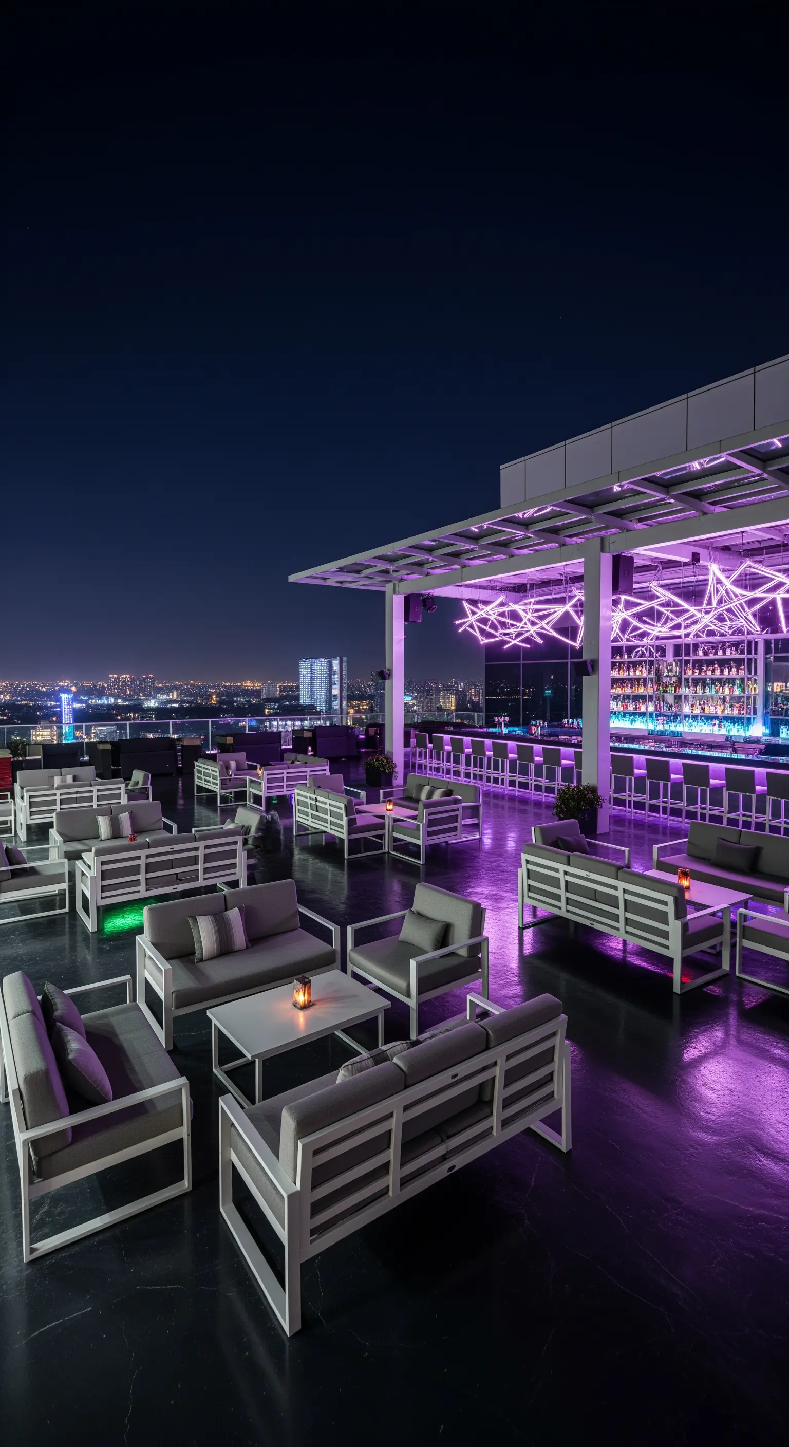 Rooftop bar con illuminazione viola, divani grigi e skyline notturno.