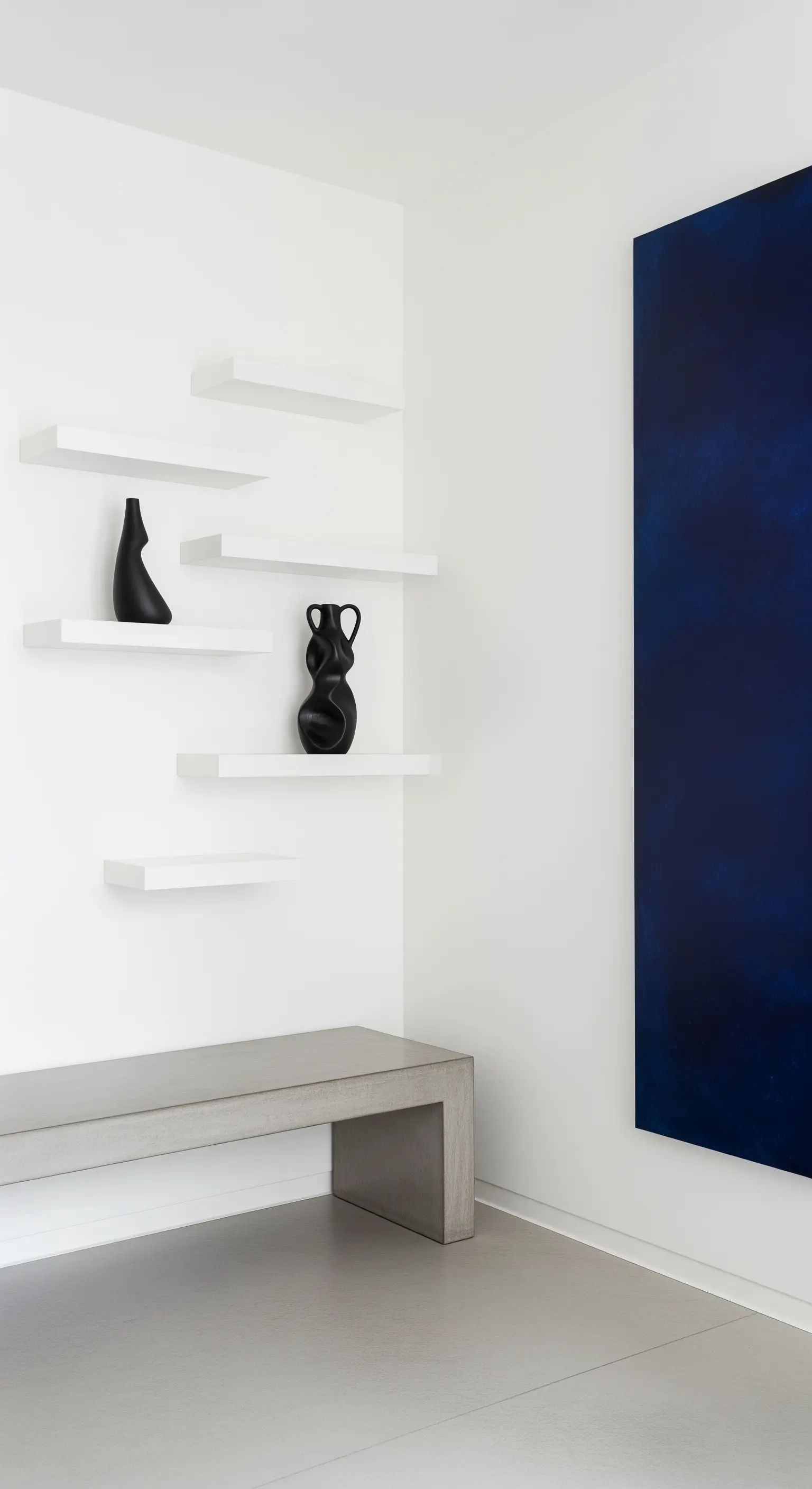 Ambiente minimalista con mensole bianche sfalsate, panca in cemento e grande tela blu notte.