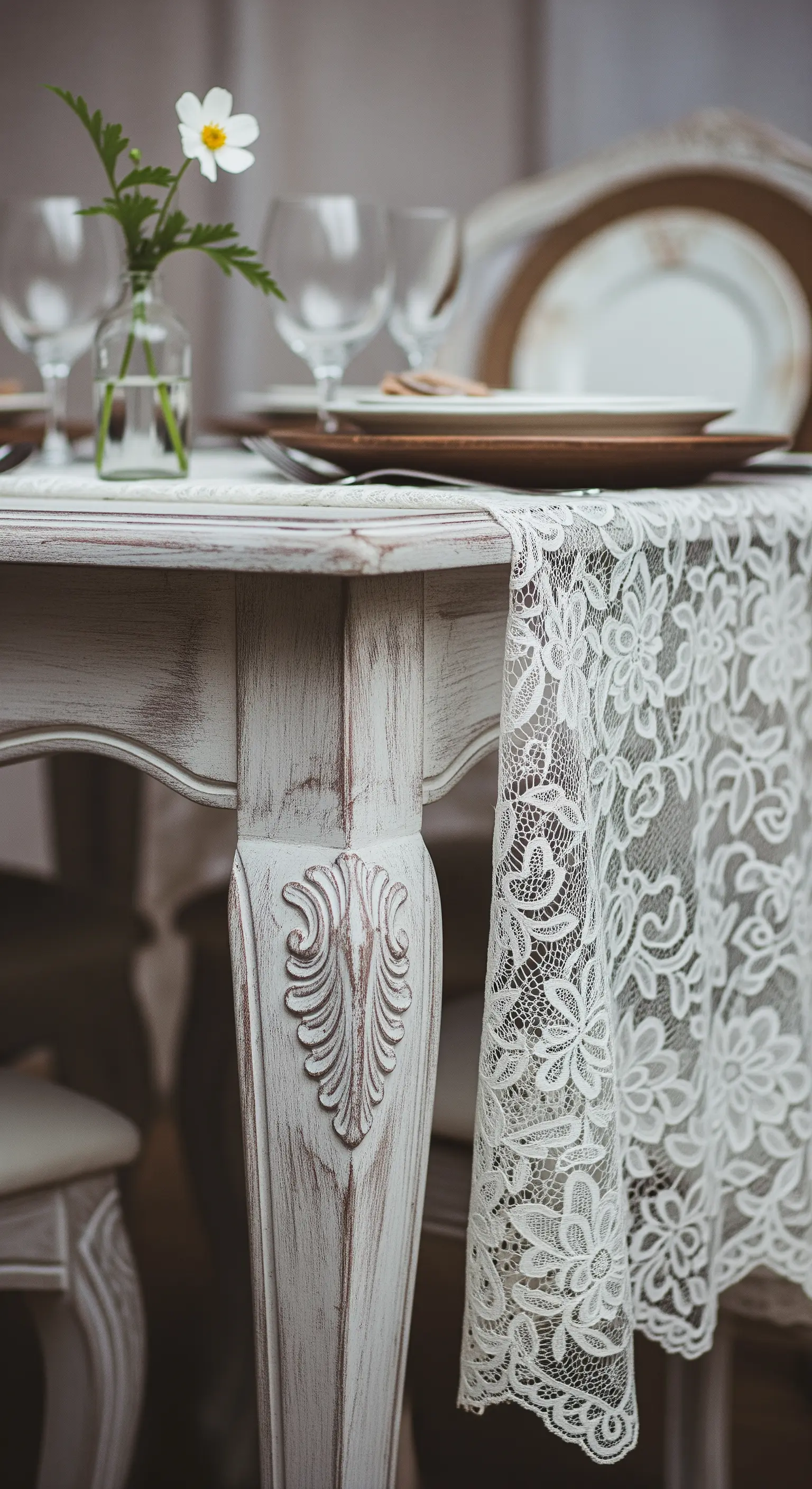 Dettaglio della gamba intagliata di un tavolo bianco decapato con un runner di pizzo che pende