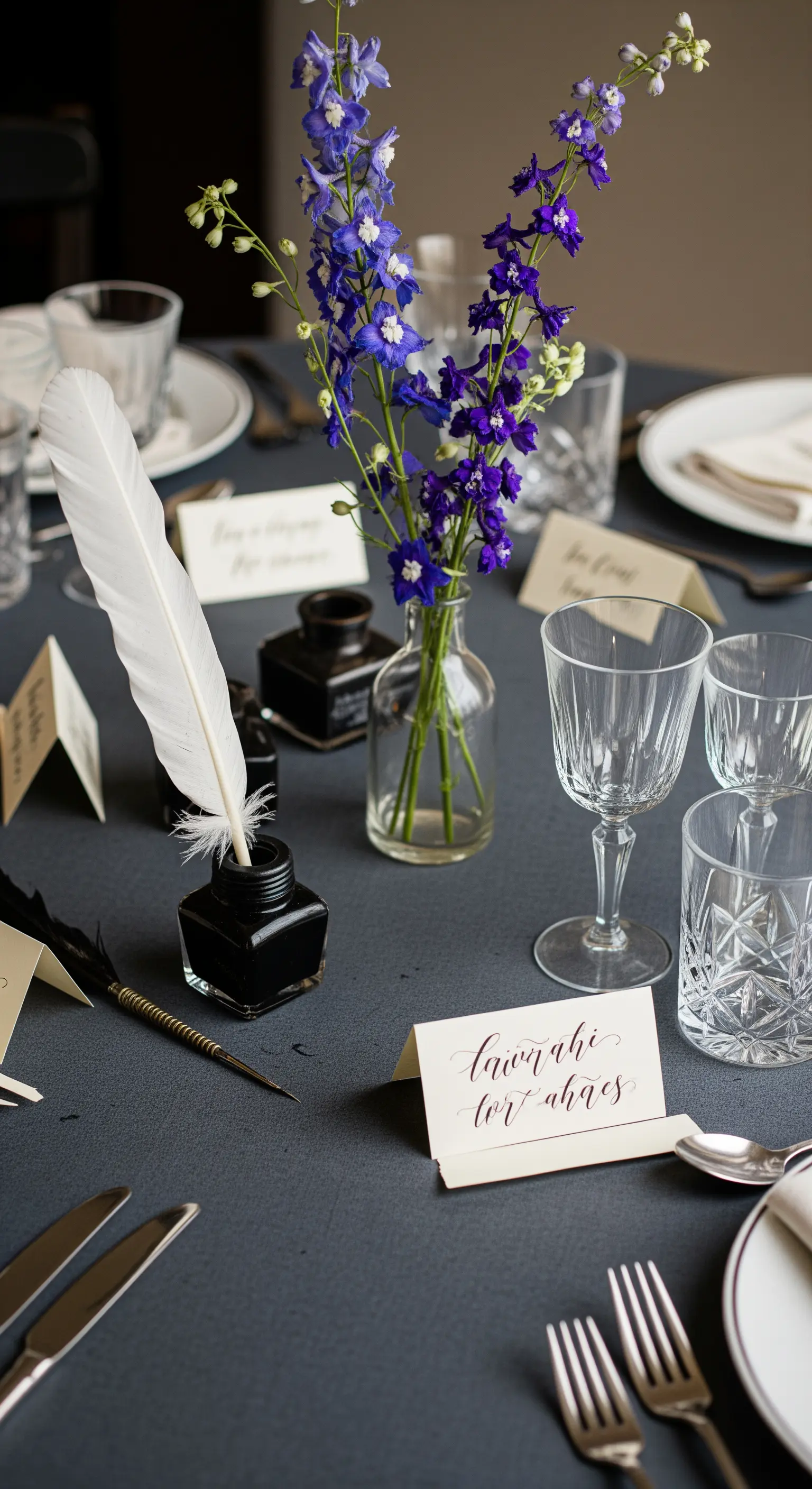 Tavola grigio scuro con segnaposto calligrafati, calamaio e fiori blu.