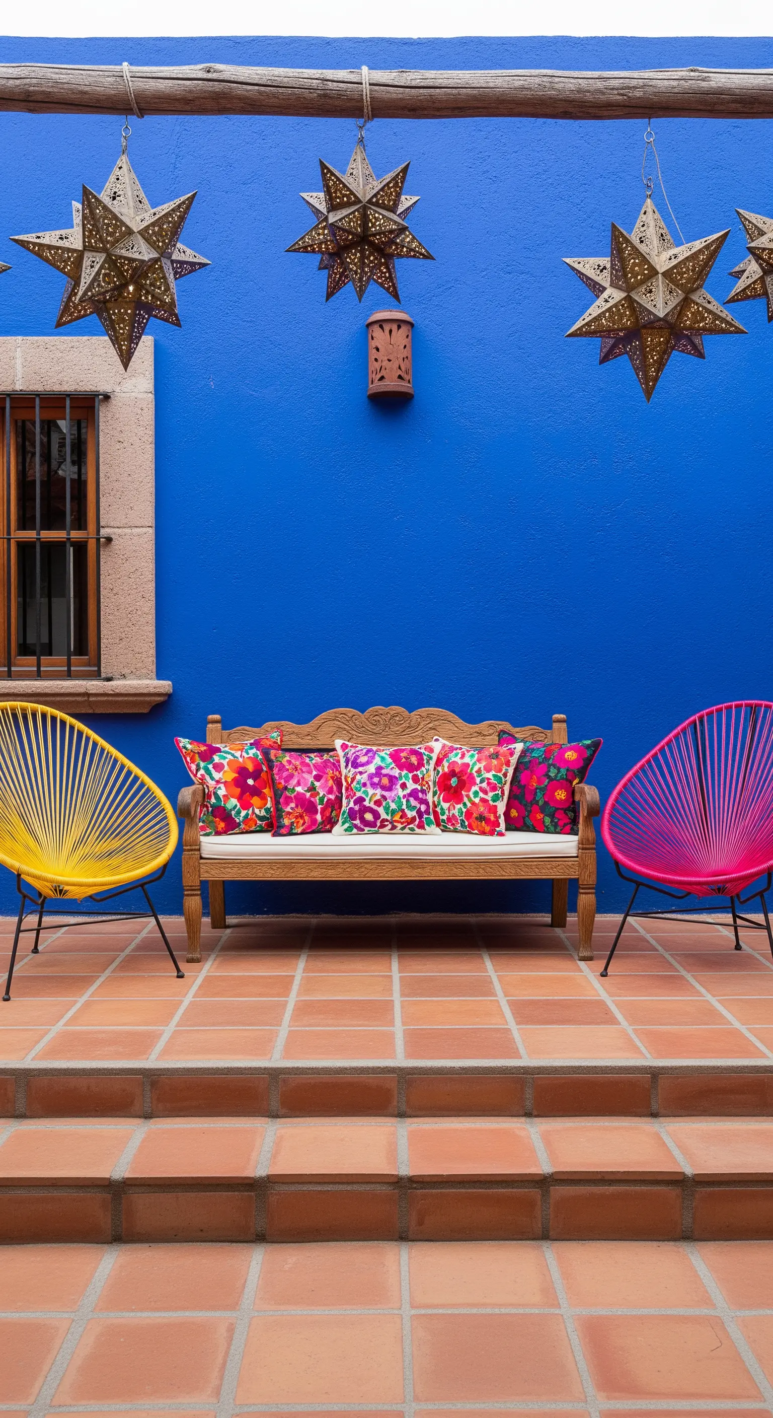 Patio con muro blu cobalto, sedie Acapulco gialla e fucsia e cuscini ricamati.