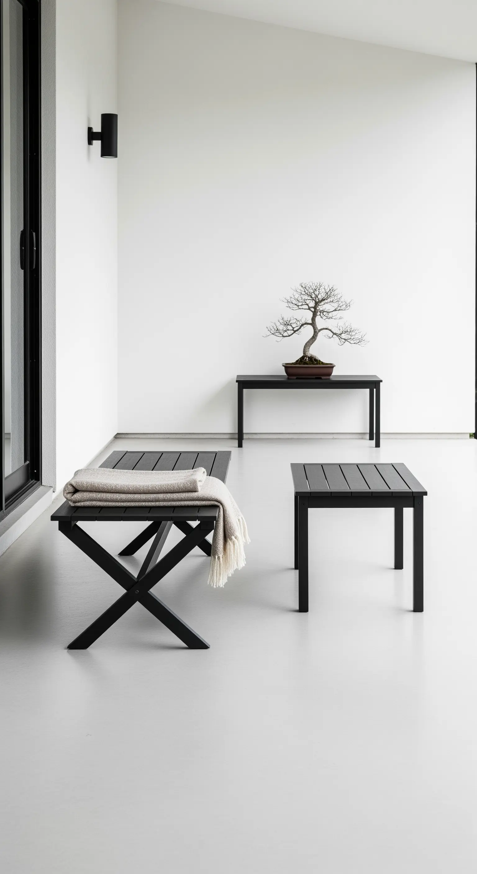Spazio esterno minimalista con panche nere, tavolini e un bonsai come punto focale.