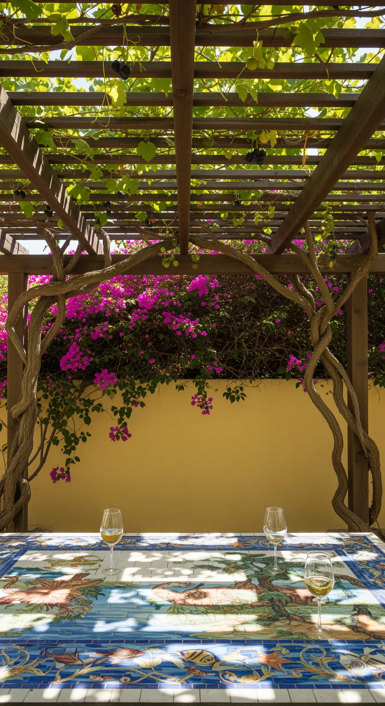 Dettaglio di un tavolo in mosaico con motivi marini sotto un pergolato di legno.