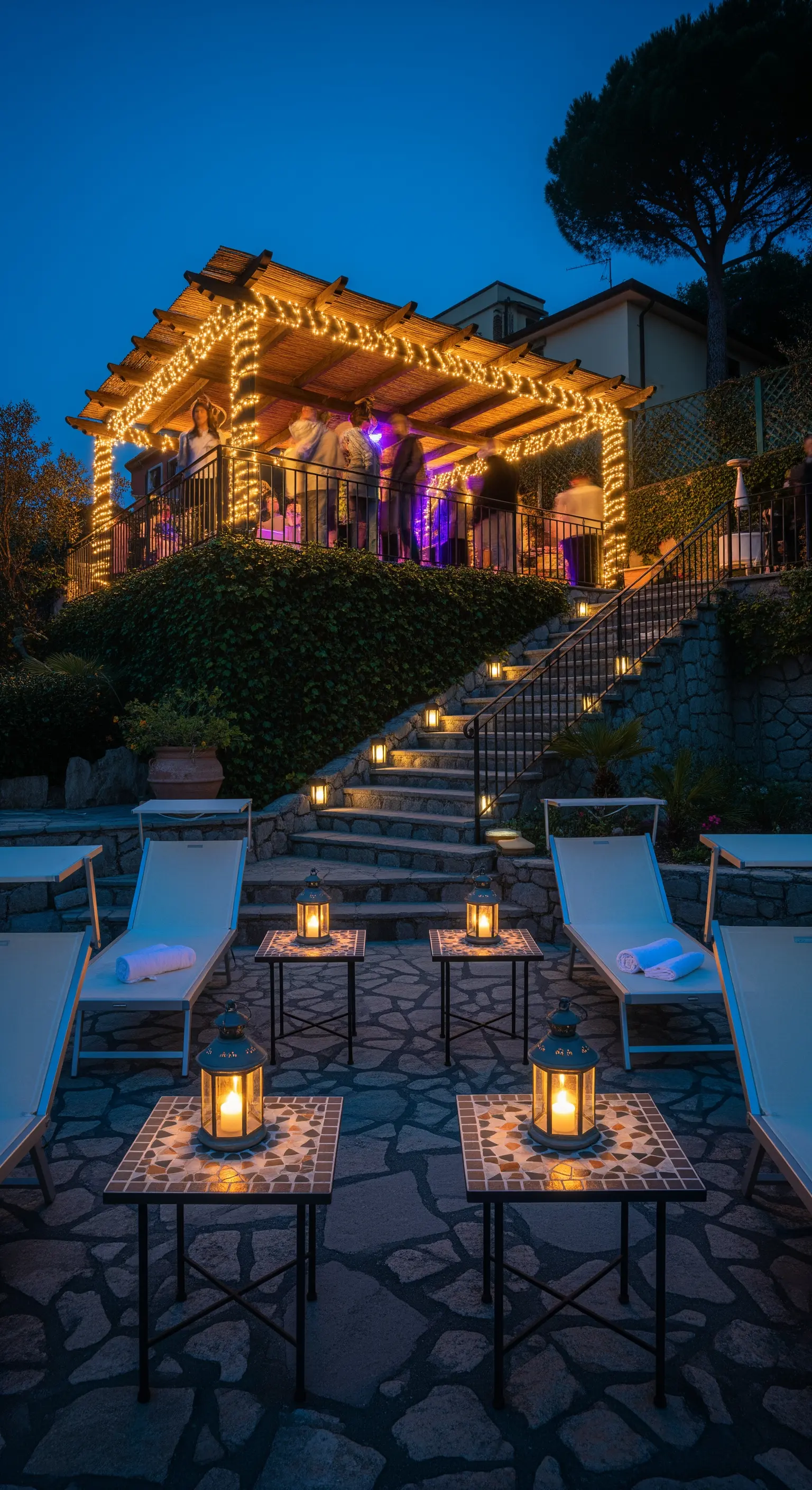 Giardino su più livelli con un pergolato illuminato, scale con faretti e area relax con lanterne