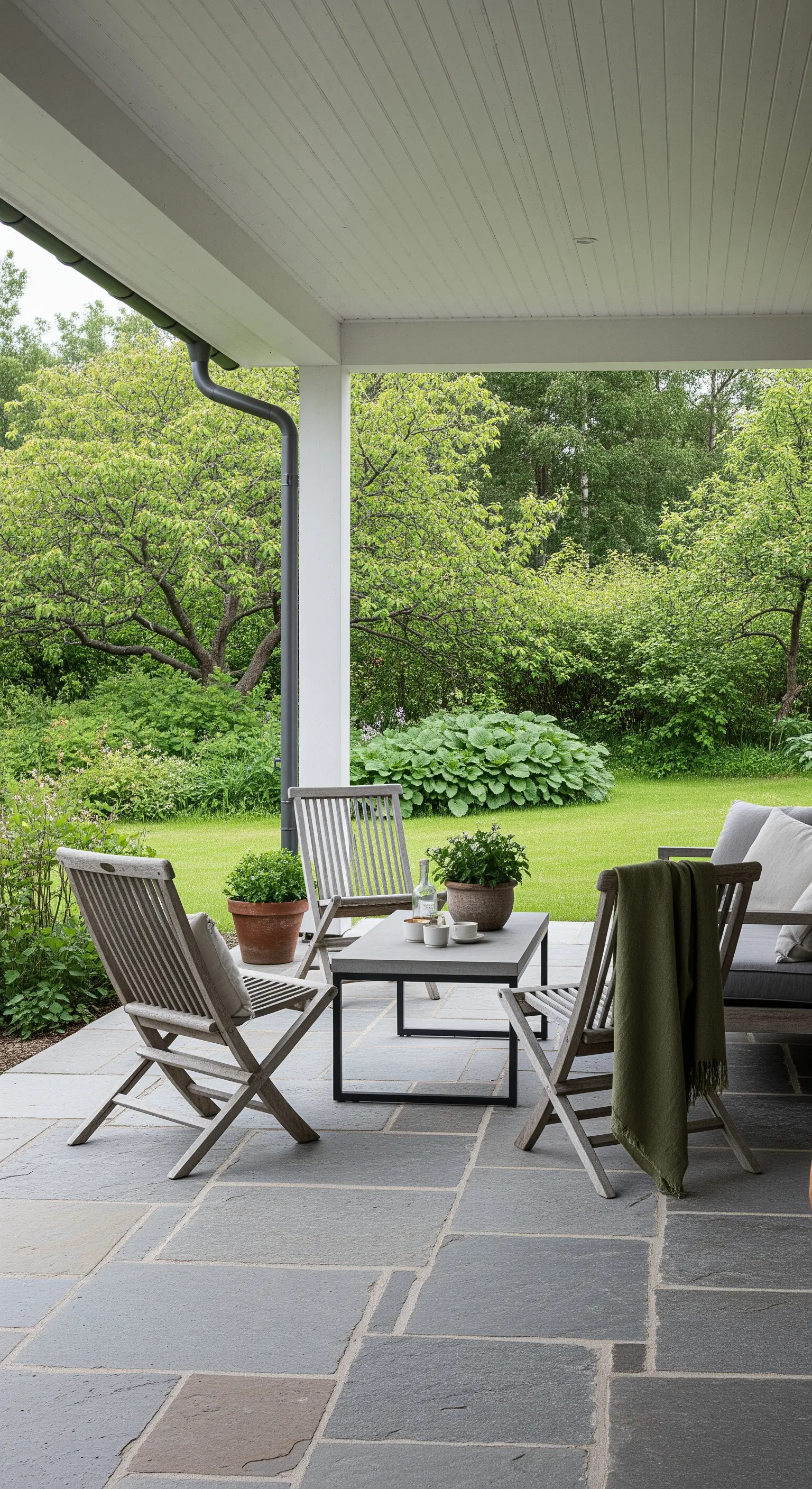 Portico con pavimento in pietra, sedie pieghevoli in legno e vista su un giardino lussureggiante.