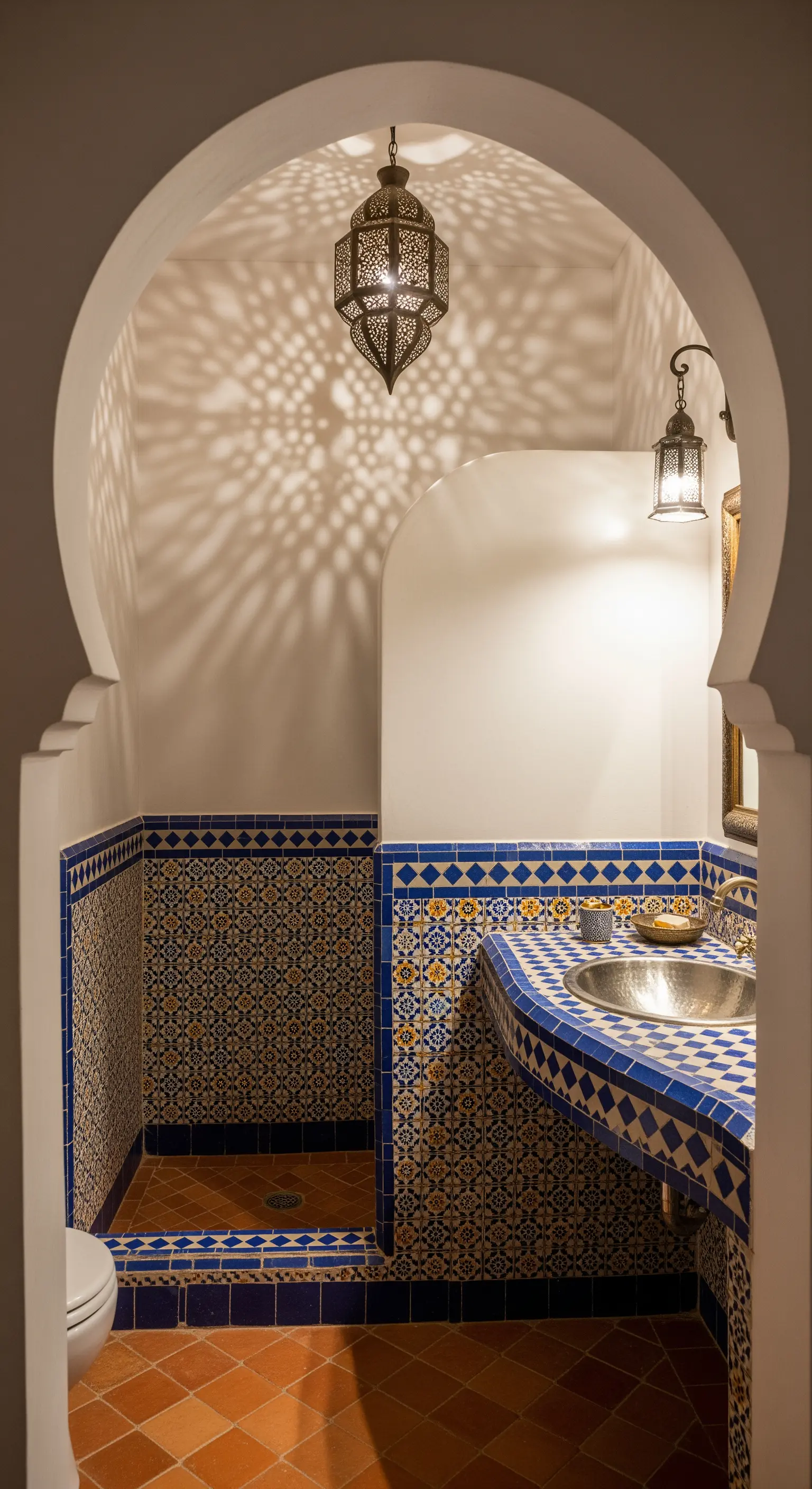 Bagno in stile marocchino con piastrelle zellige, lavabo in metallo e lanterna traforata.