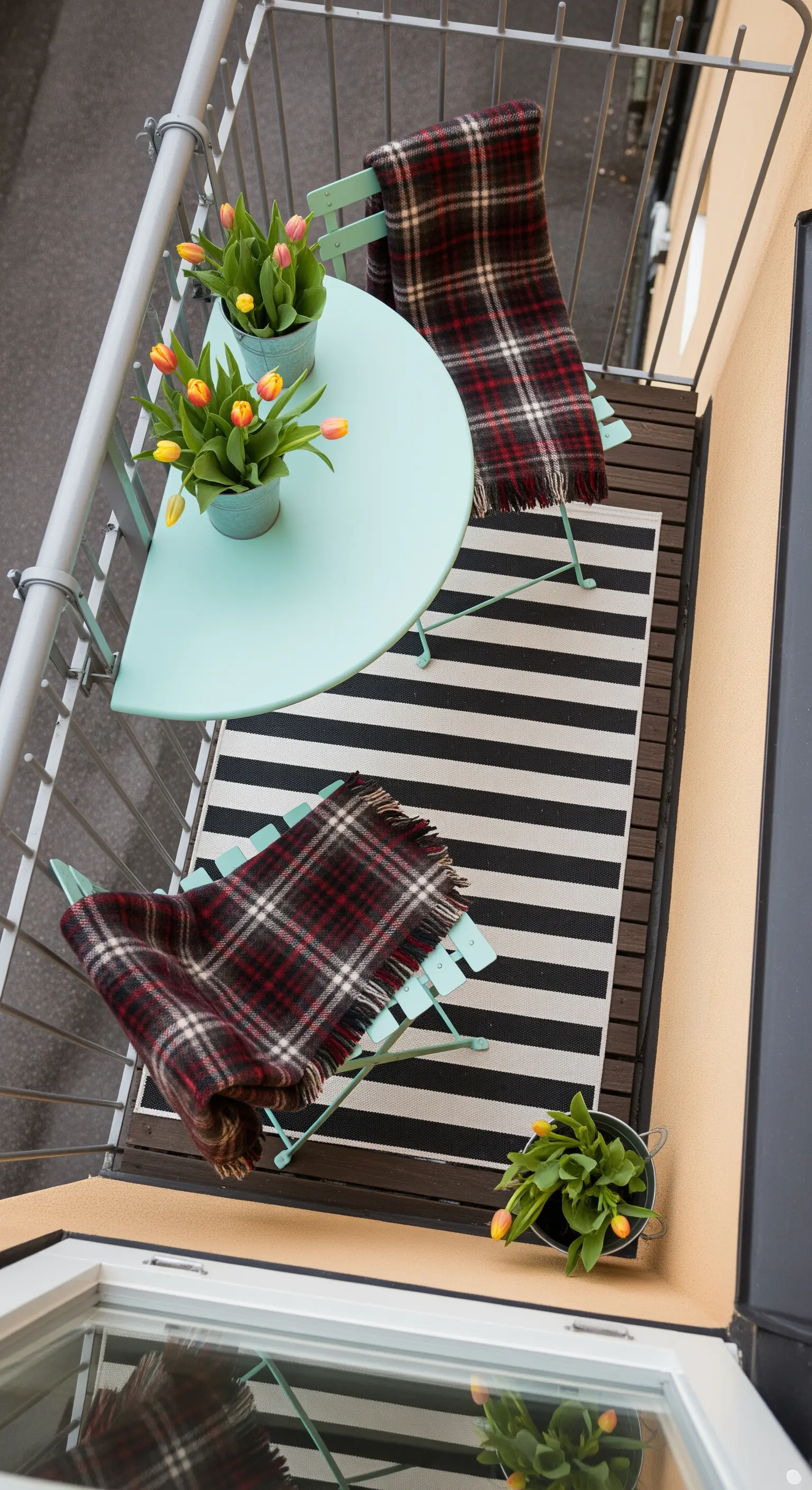Vista dall'alto di un balcone con set da bistrò verde menta, tappeto a righe e plaid scozzesi.
