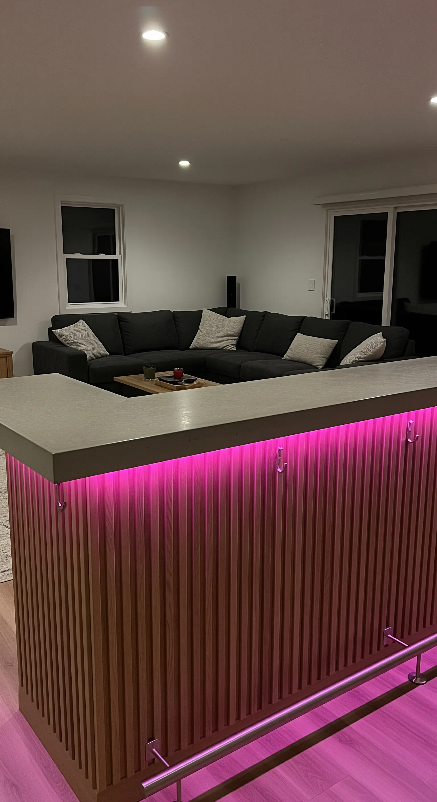 Bancone bar con top in cemento e base in legno, illuminato da una striscia LED rosa.