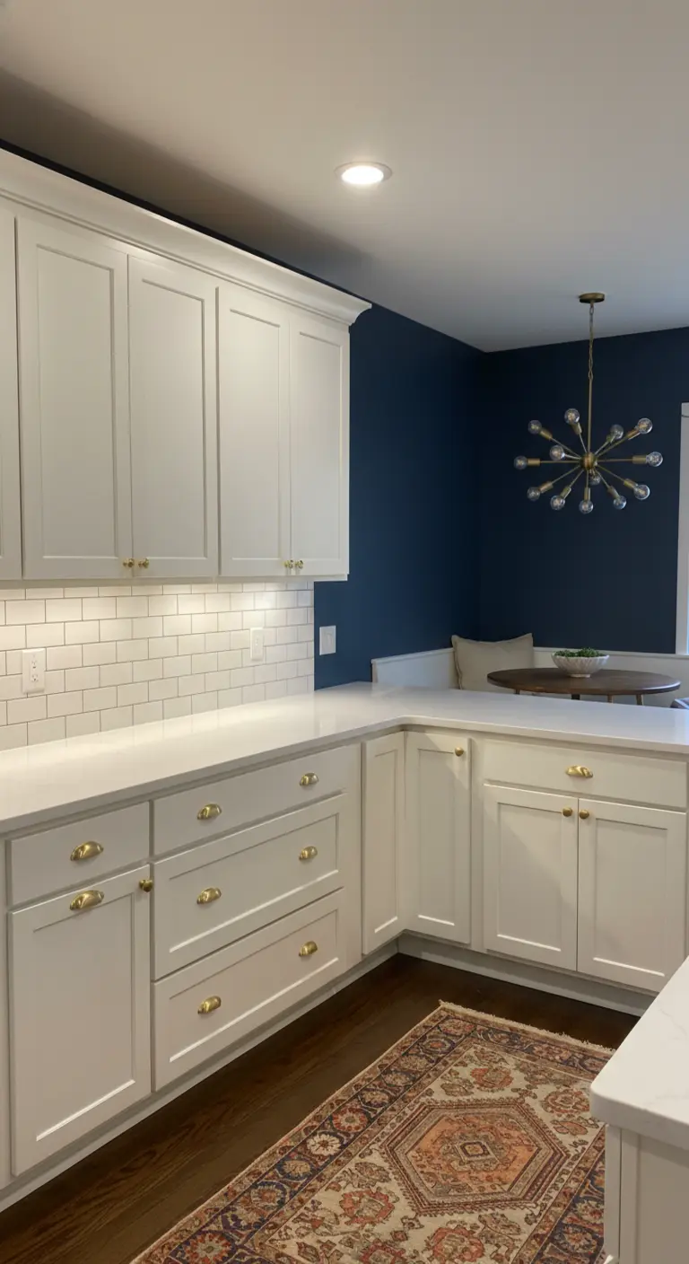 Cucina bianca con parete blu navy, maniglie dorate e lampadario a sputnik nell'angolo pranzo.