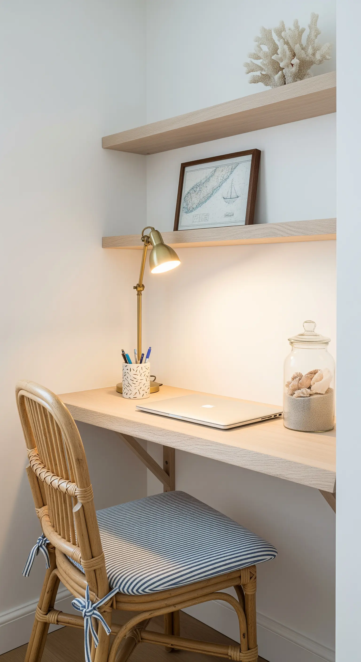 Scrivania minimalista in legno chiaro con sedia in rattan e lampada in ottone.