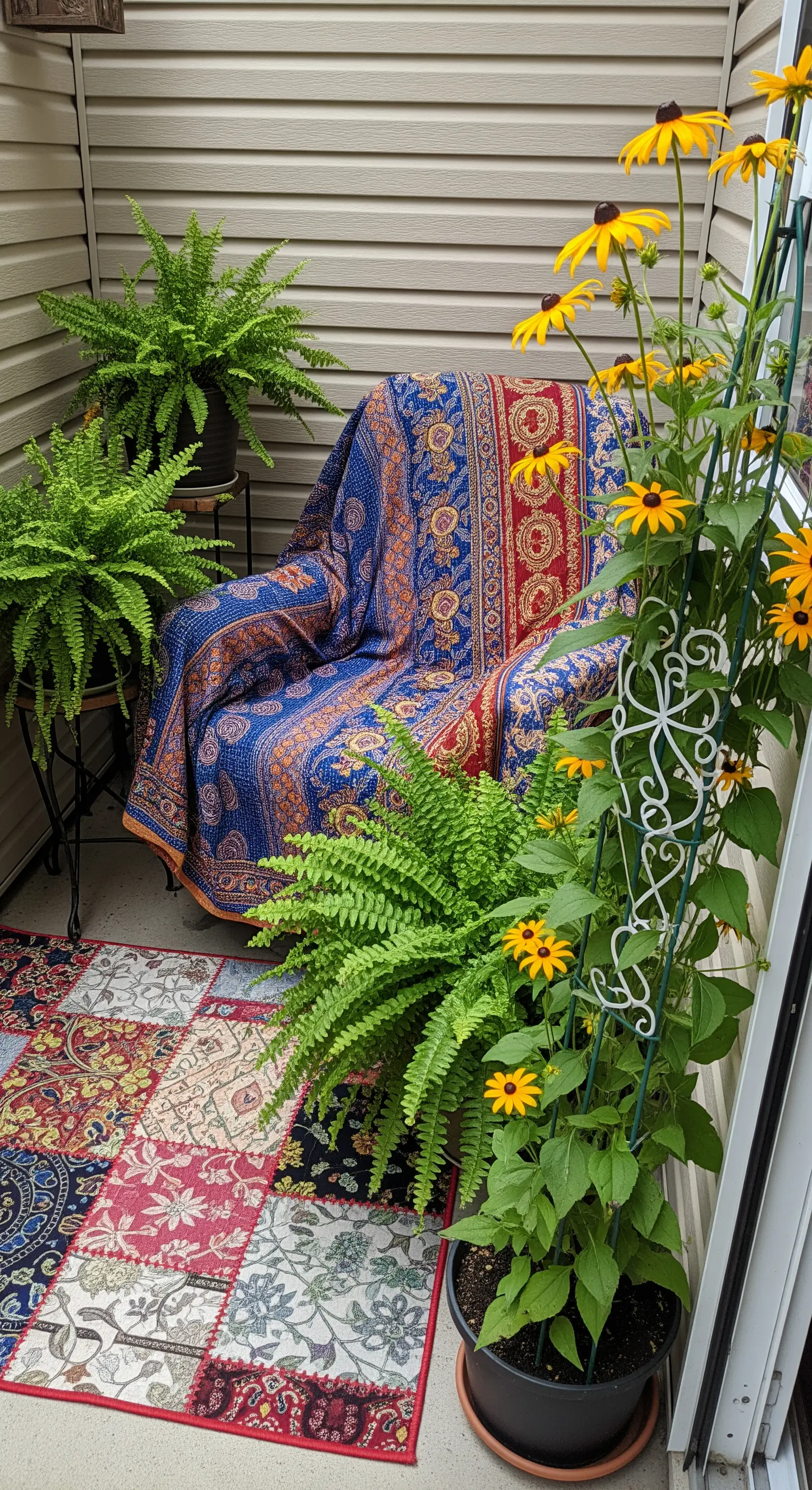 Angolo di un balcone con poltrona coperta da una trapunta kantha, circondata da felci e fiori.