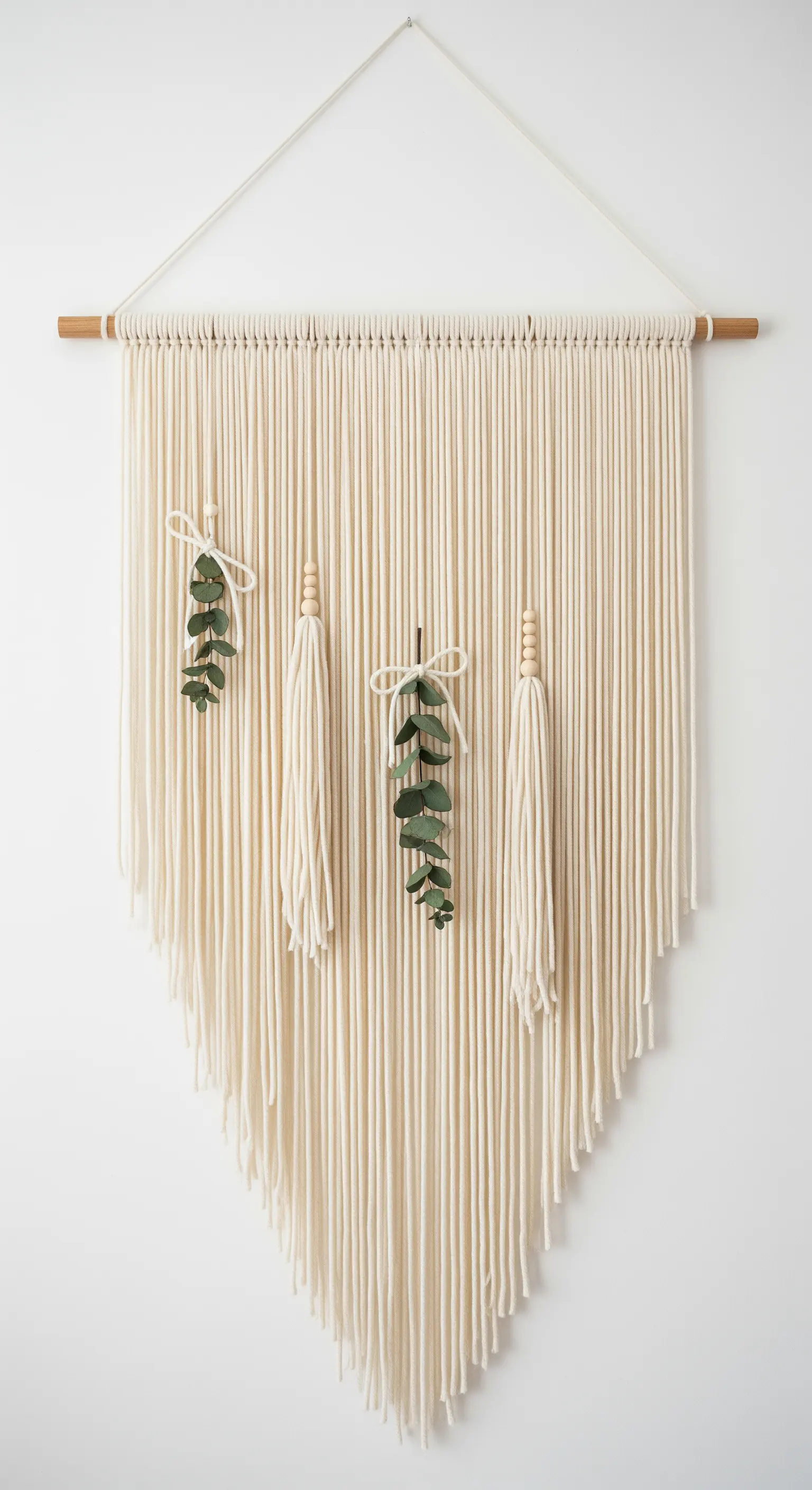 Arazzo in macramè appeso a una parete bianca, decorato con rametti di eucalipto.