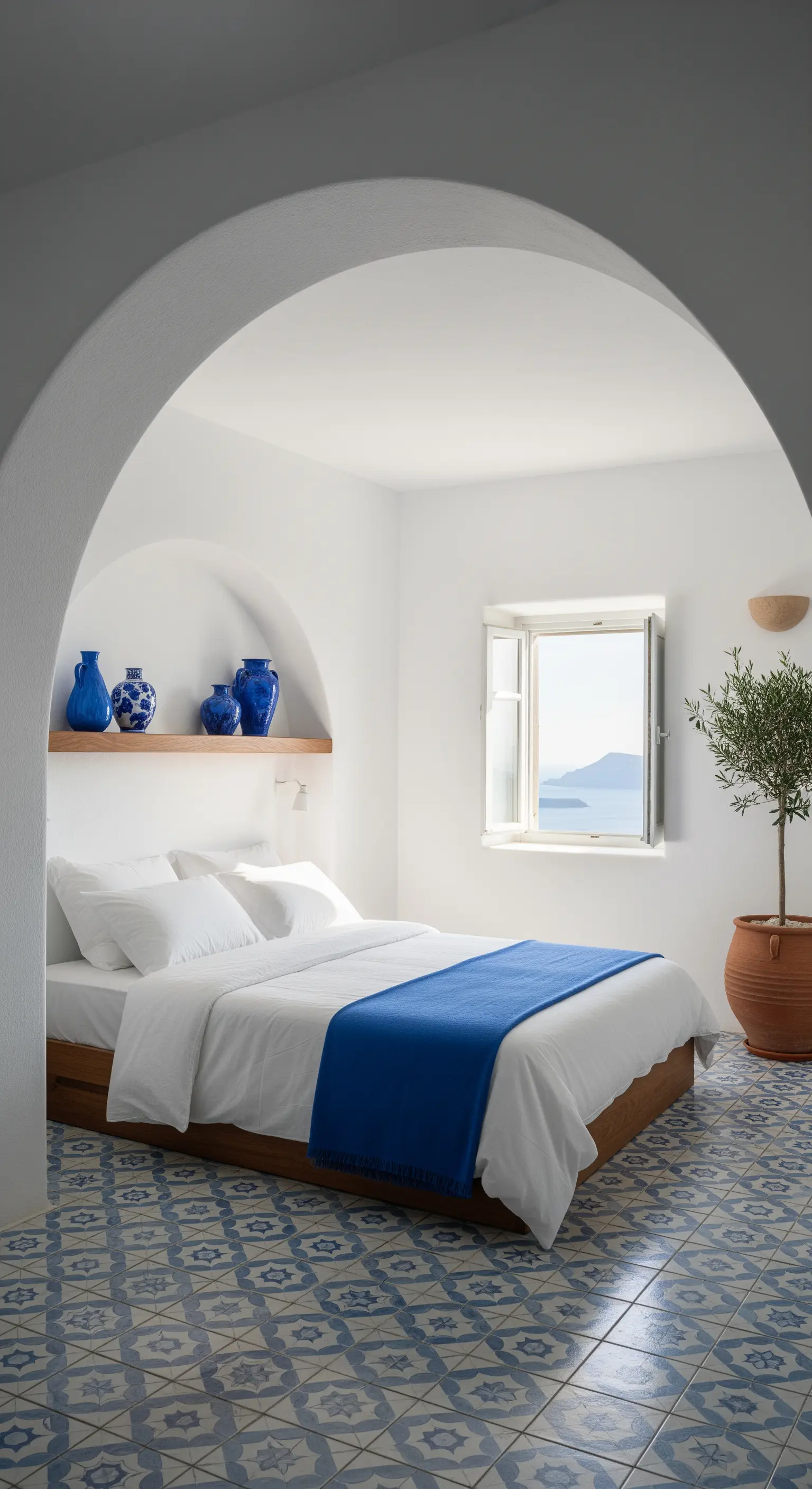 Camera da letto con arco, pareti bianche, pavimento in maiolica blu e vista mare.