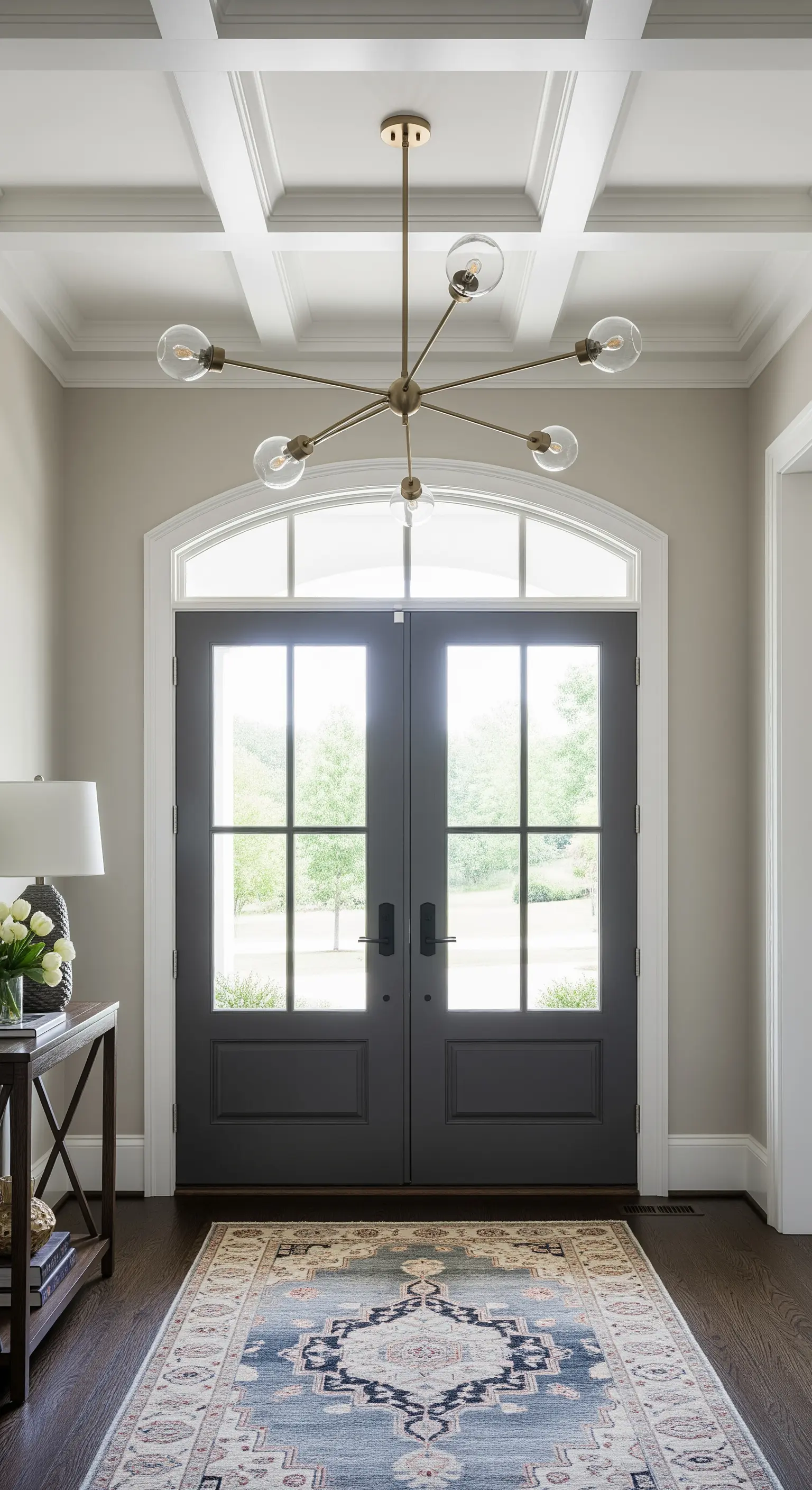 Ingresso con soffitto a cassettoni, porte scure e lampadario moderno in ottone.