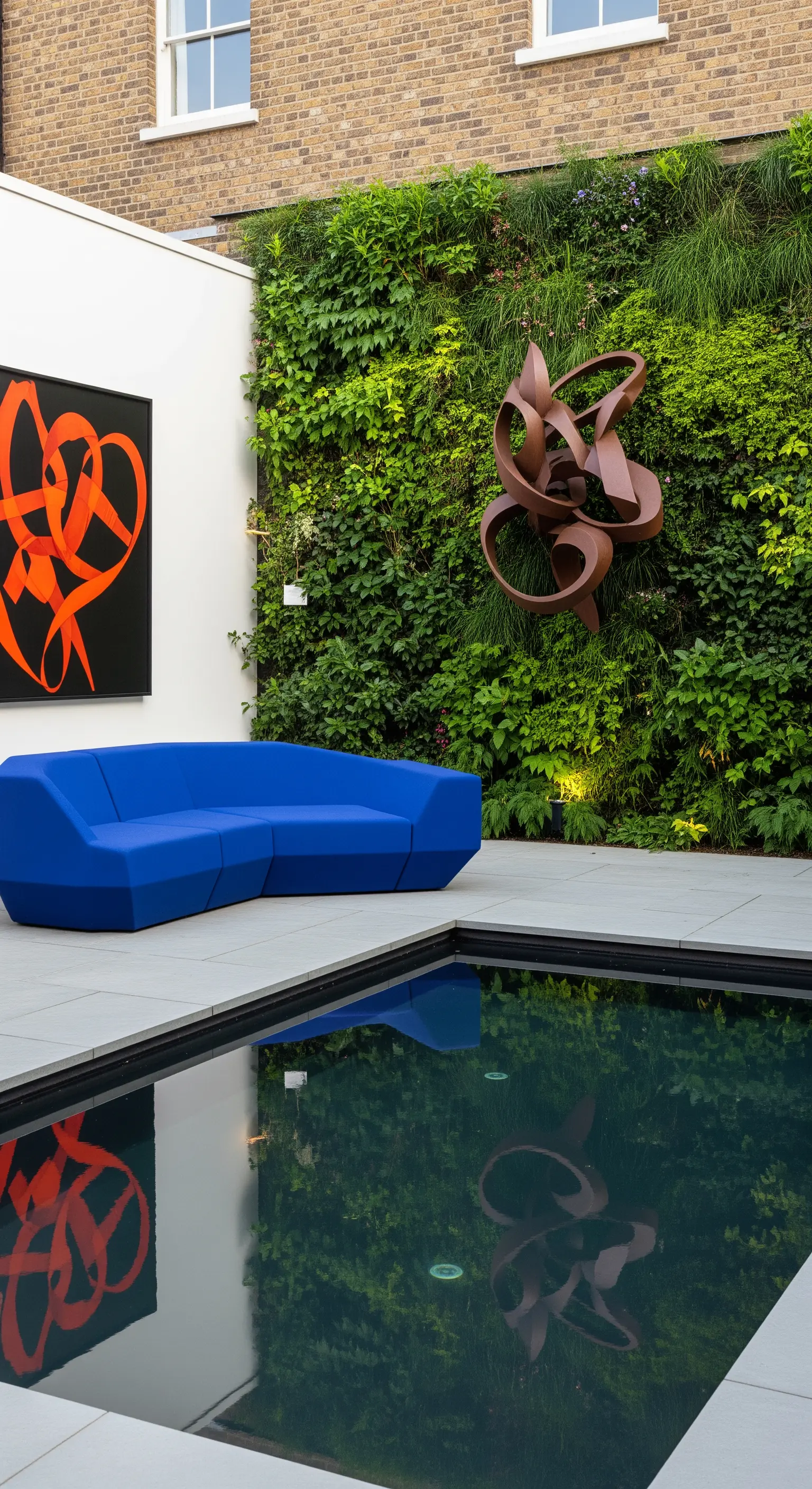 Patio con divano blu, quadro astratto e scultura in metallo su una parete verde.