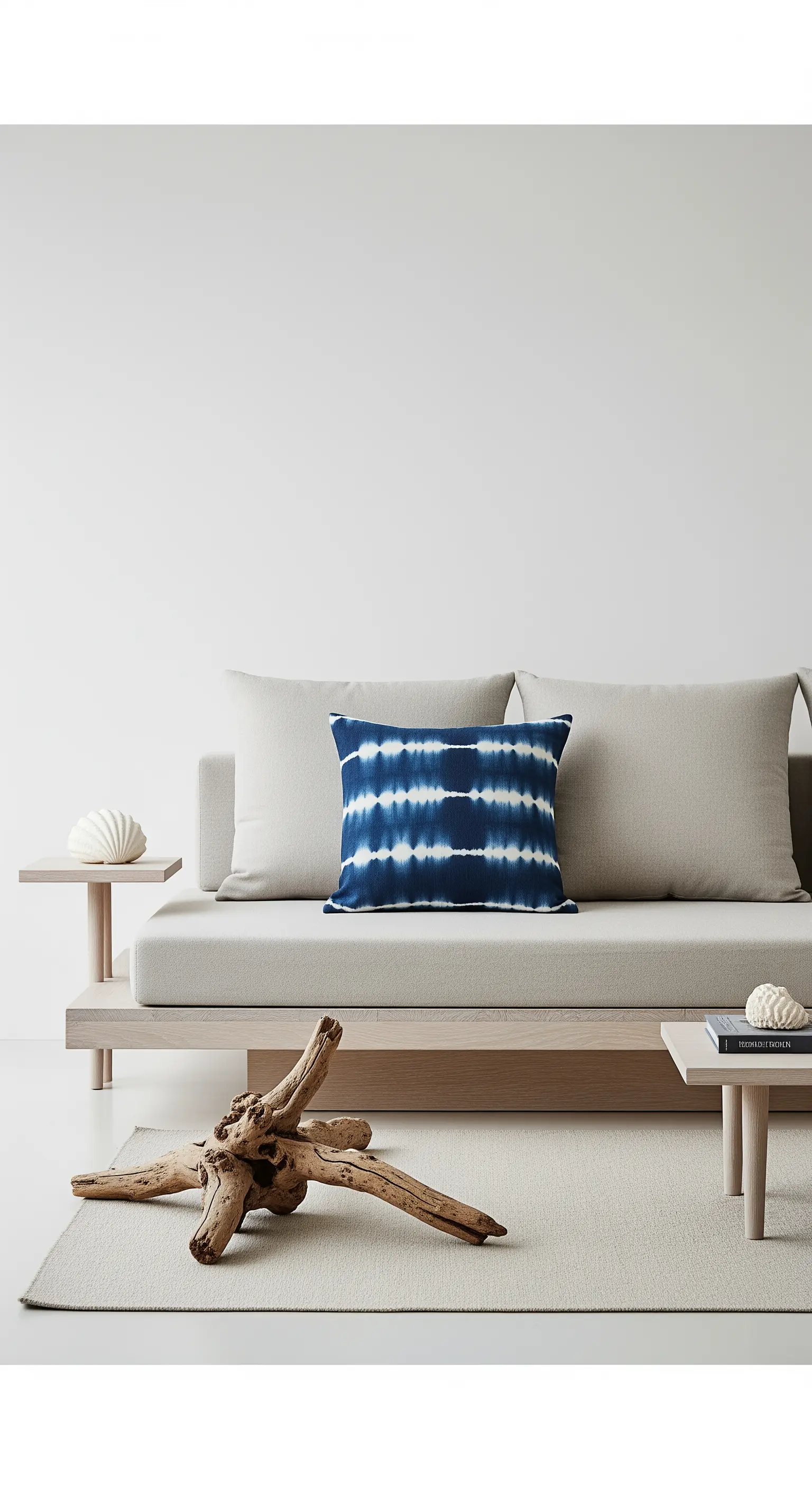 Ambiente minimalista con divano basso, un pezzo di legno spiaggiato e un cuscino tie-dye blu.