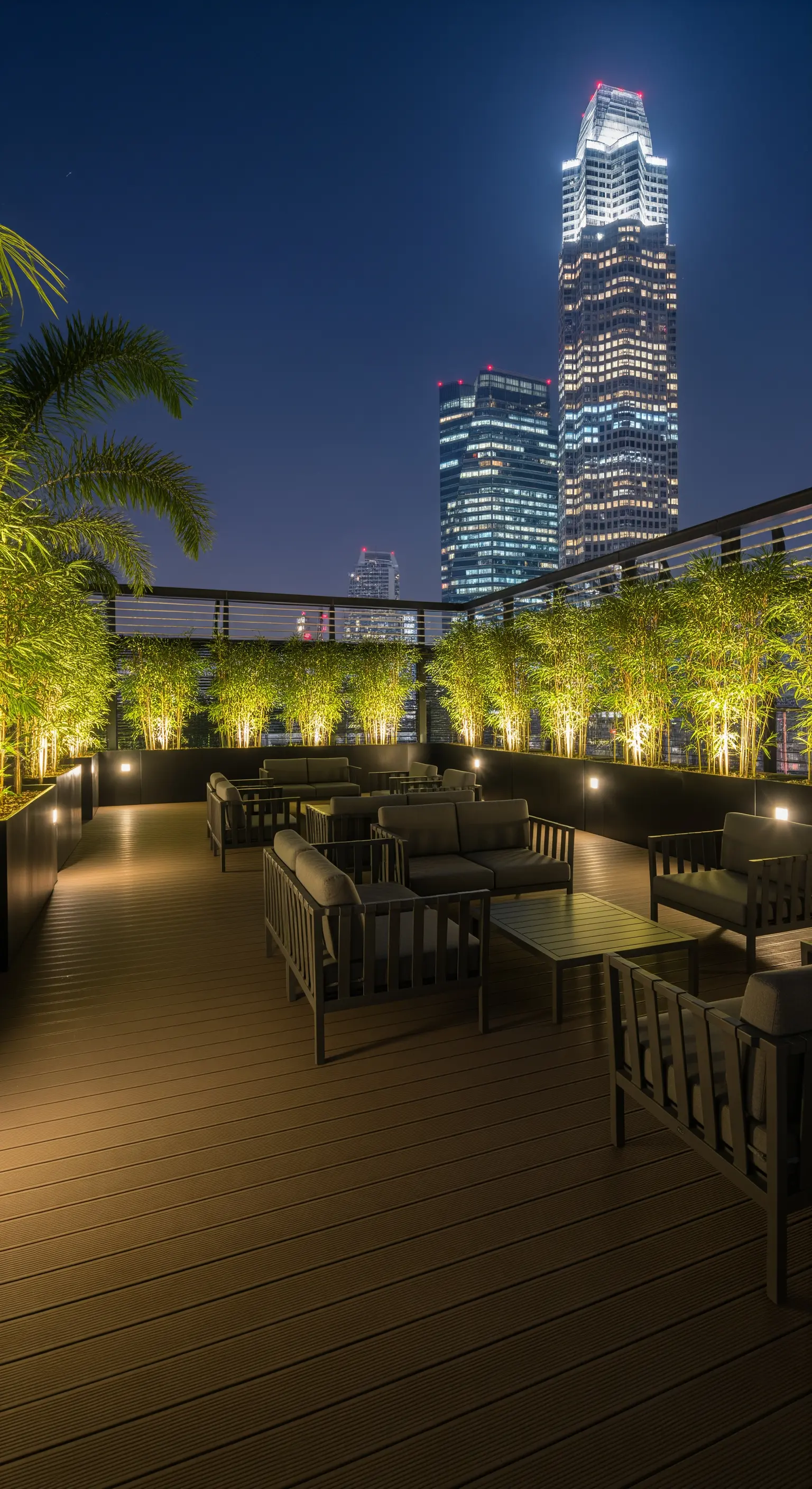 Terrazza panoramica di notte con divani scuri e piante di bambù illuminate dal basso.