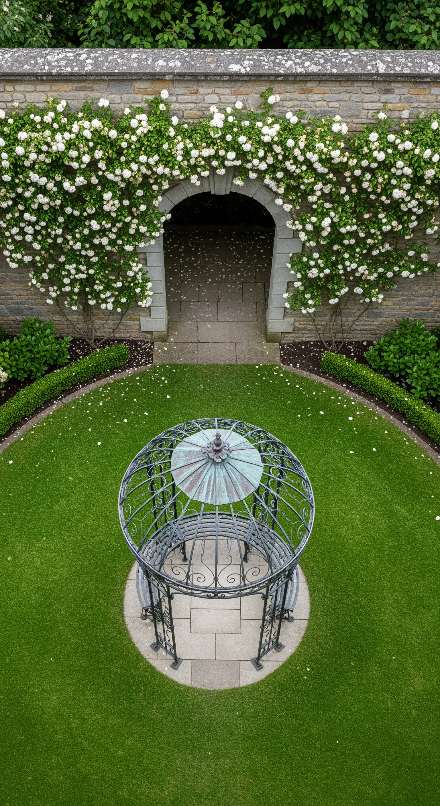 Vista aerea di un gazebo circolare in un prato perfettamente curato con un arco fiorito.