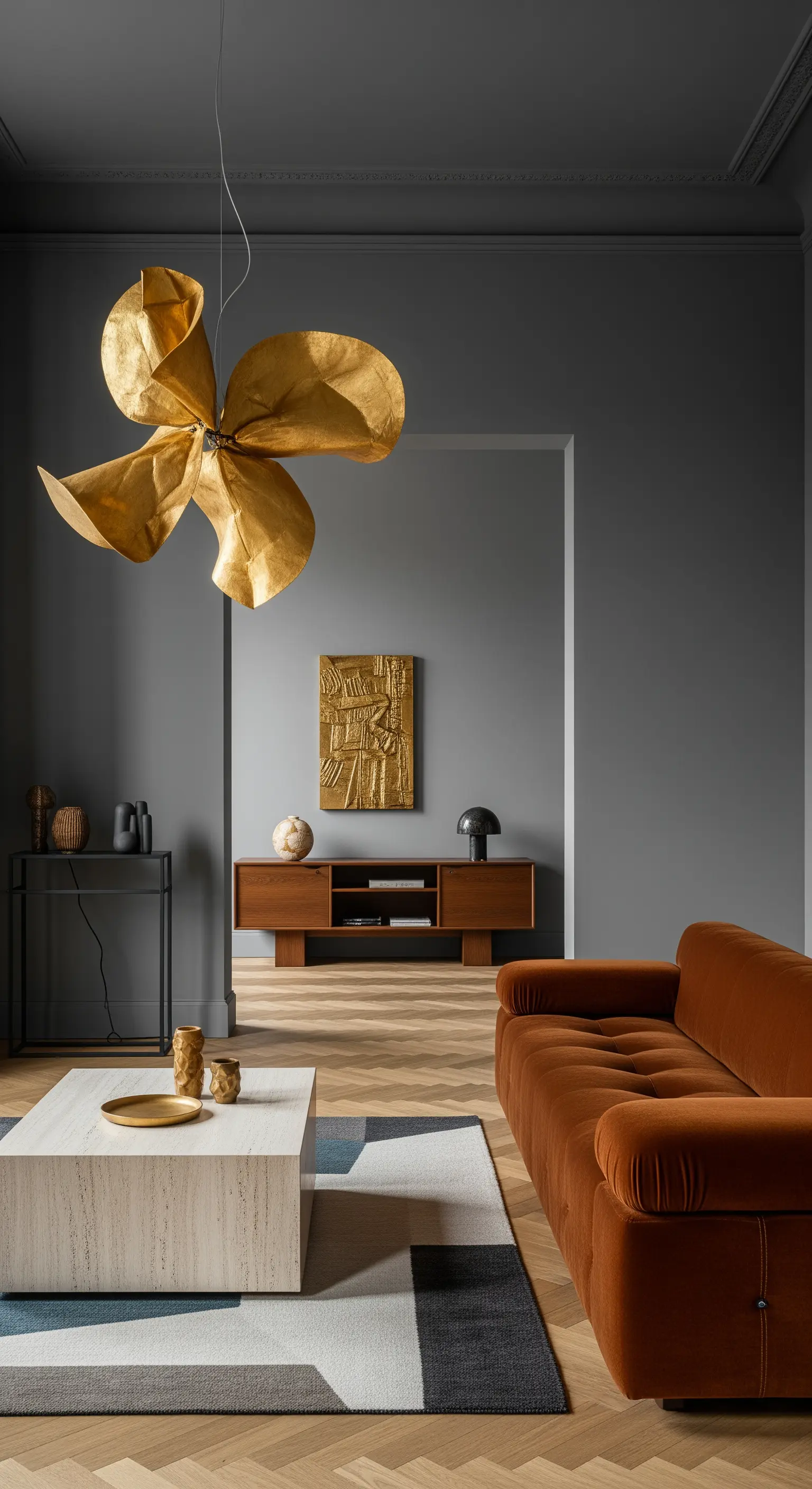 Soggiorno minimalista con pareti grigie, divano in velluto terracotta e lampadario scultoreo dorato.