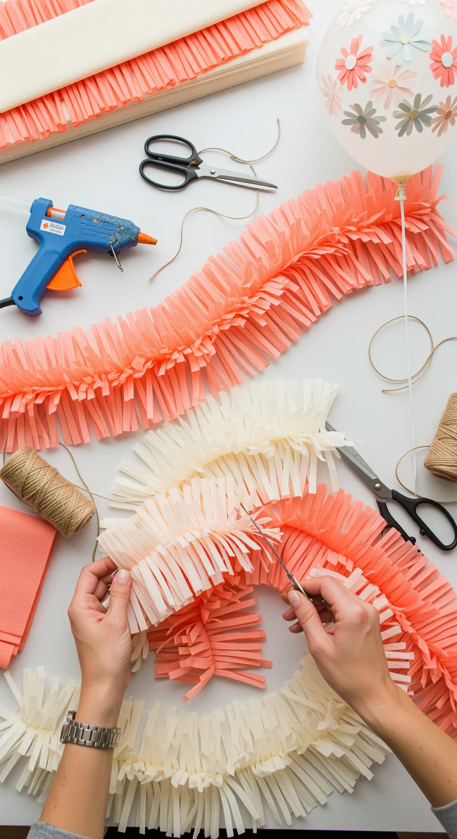 Creazione di una ghirlanda fai-da-te con frange di carta crespa color corallo e crema.