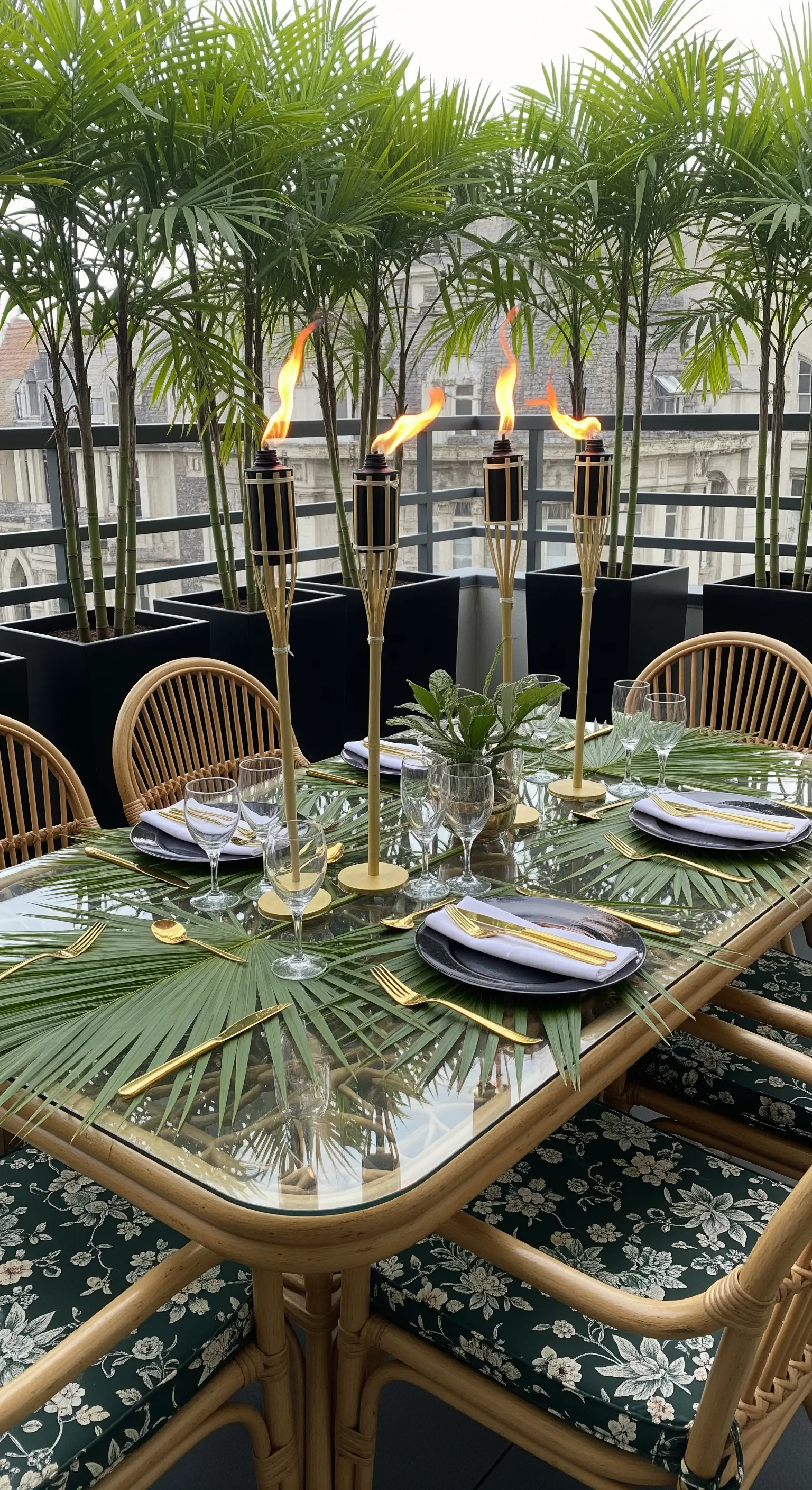 Tavolo da pranzo in vetro con foglie di palma come centrotavola e posate dorate.