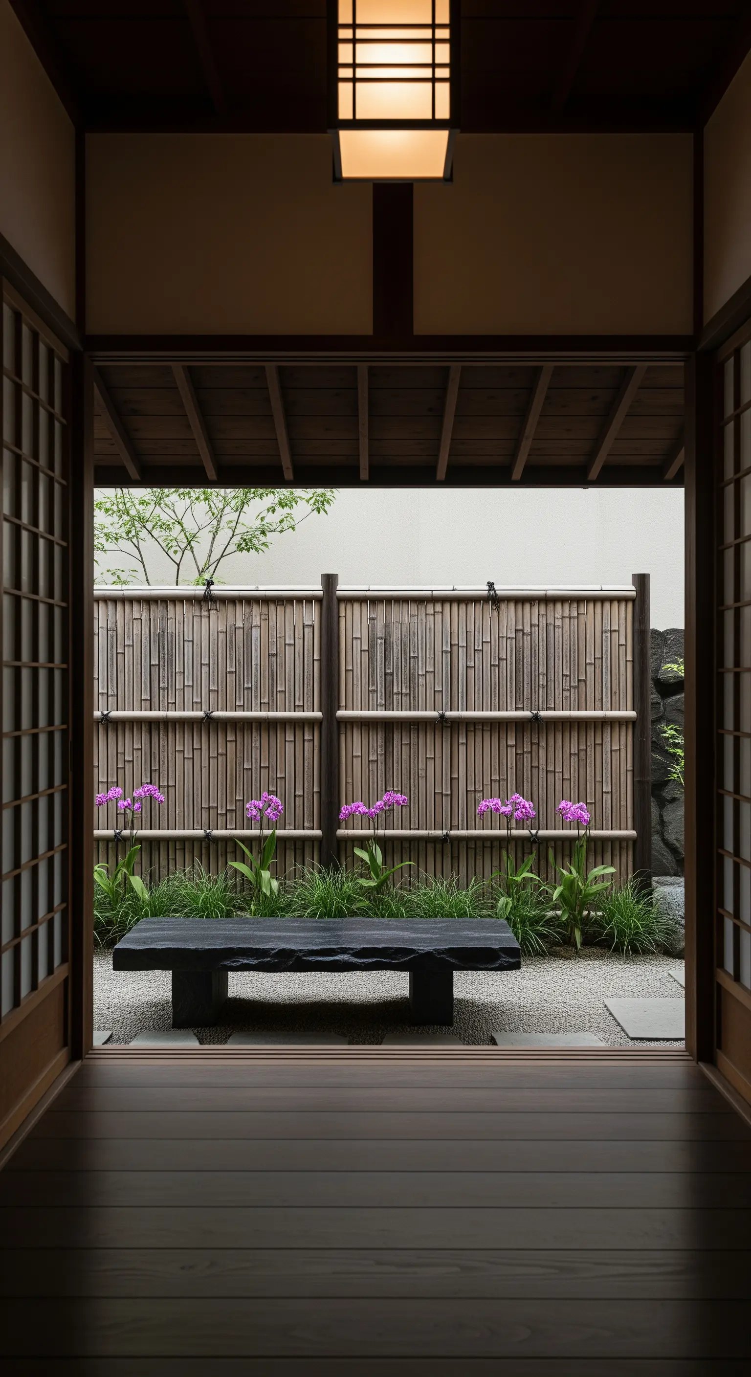Cortile interno in stile giapponese con panca in pietra nera, ghiaia e recinzione in bambù.