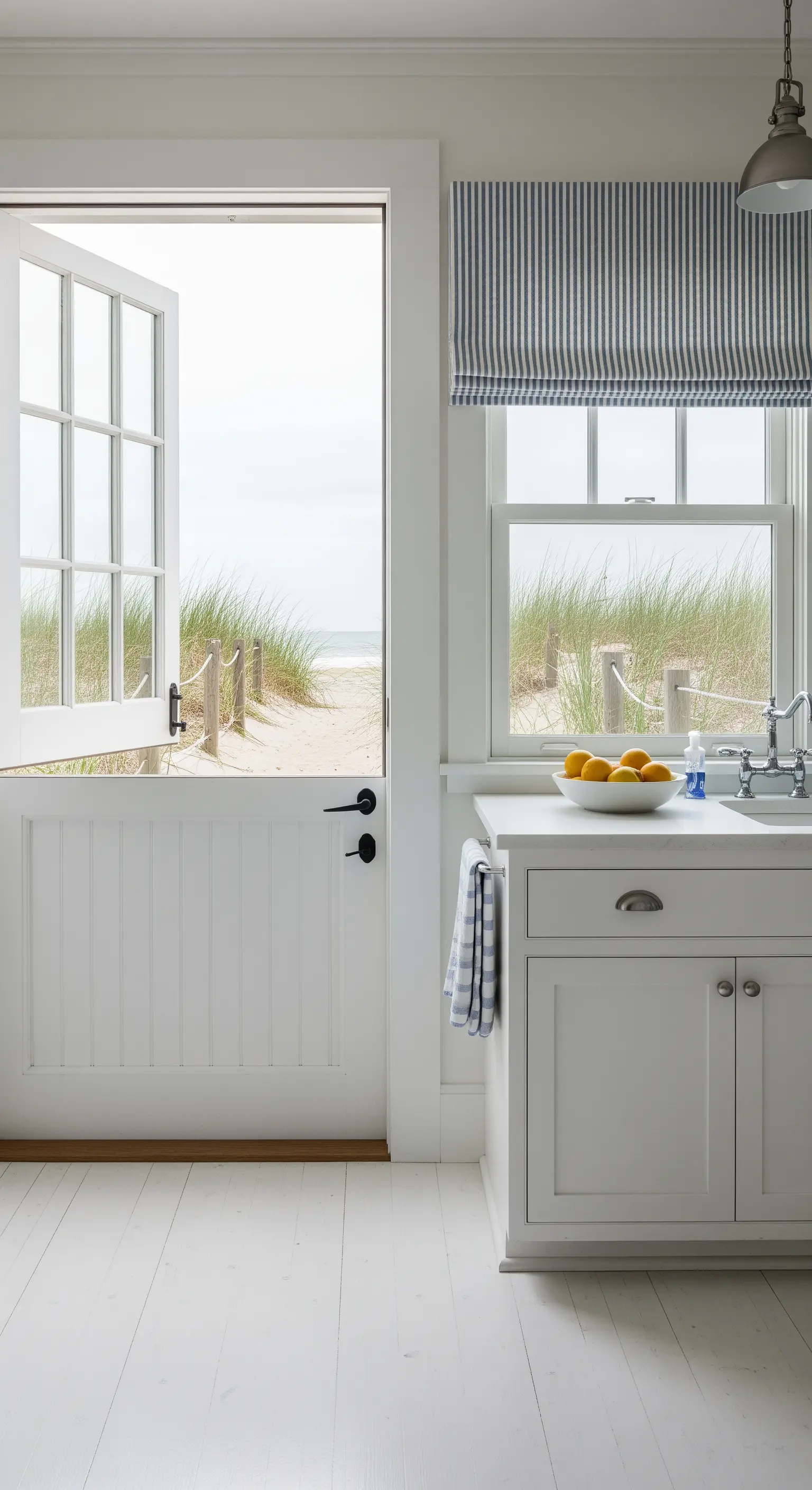 Porta olandese bianca aperta che affaccia su una spiaggia con dune di sabbia.