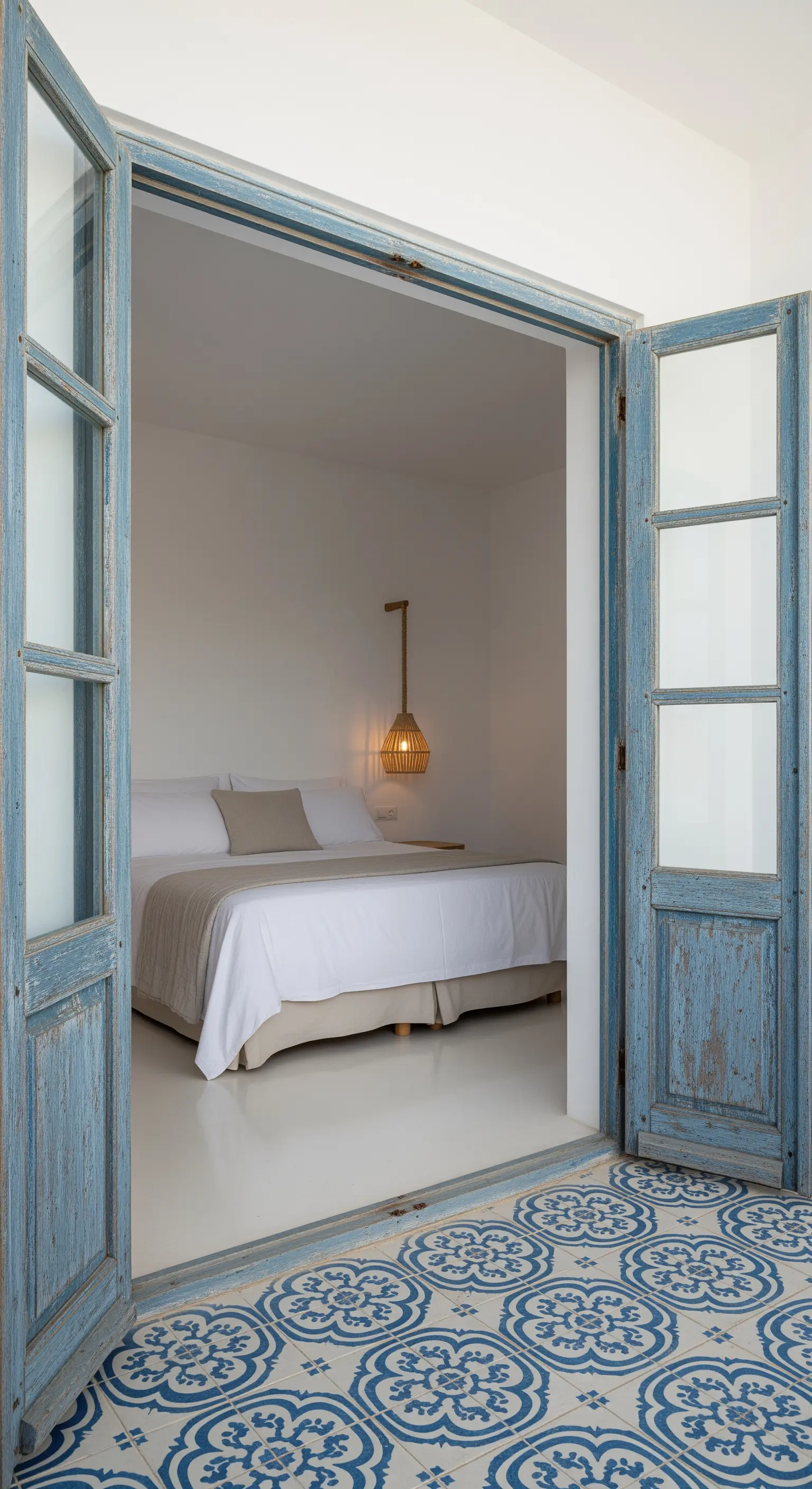 Porte doppie in legno blu invecchiato che si aprono su una camera da letto bianca.