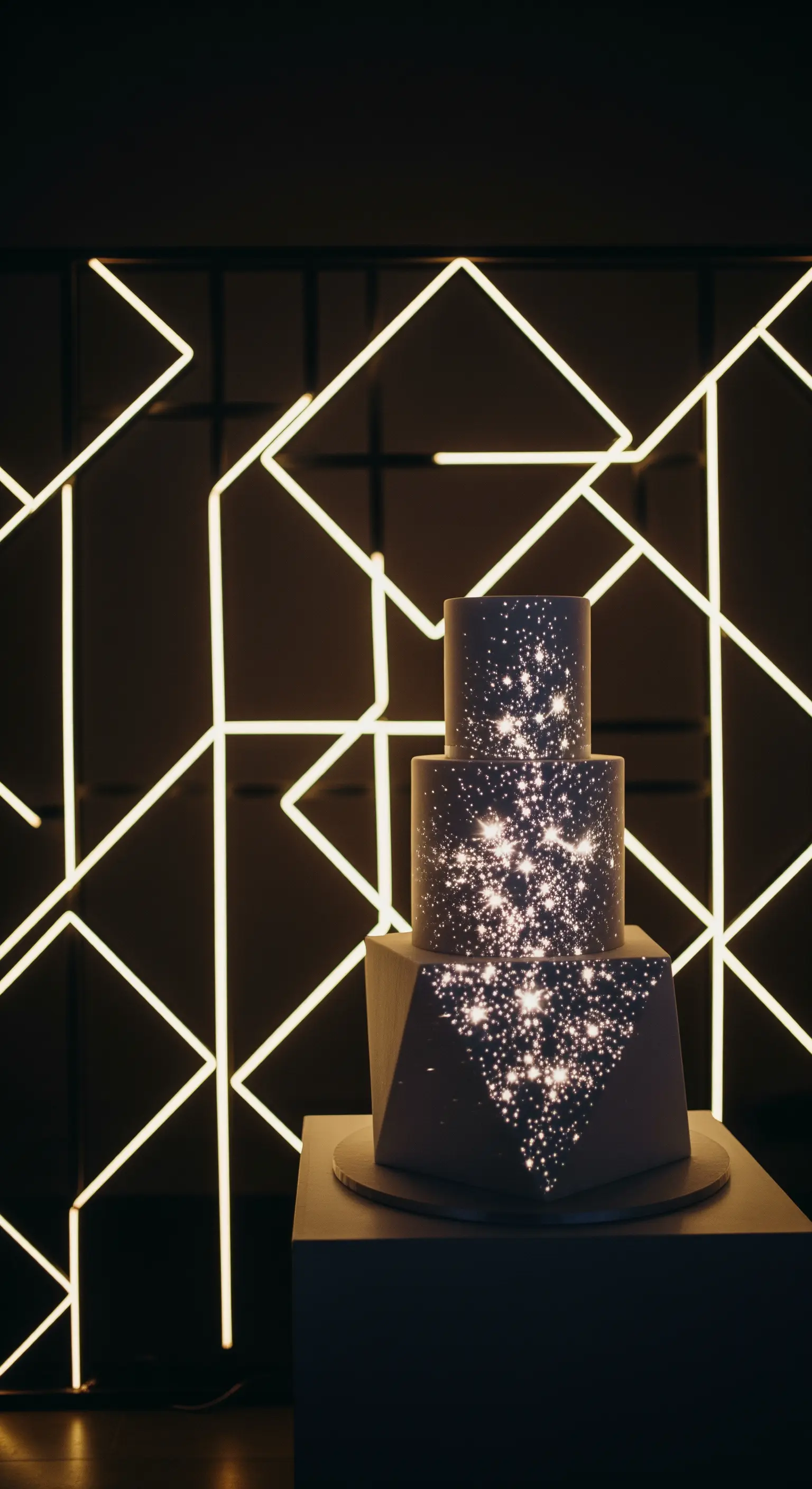 Torta nuziale scura su cui è proiettata una galassia, con sfondo di LED geometrici.