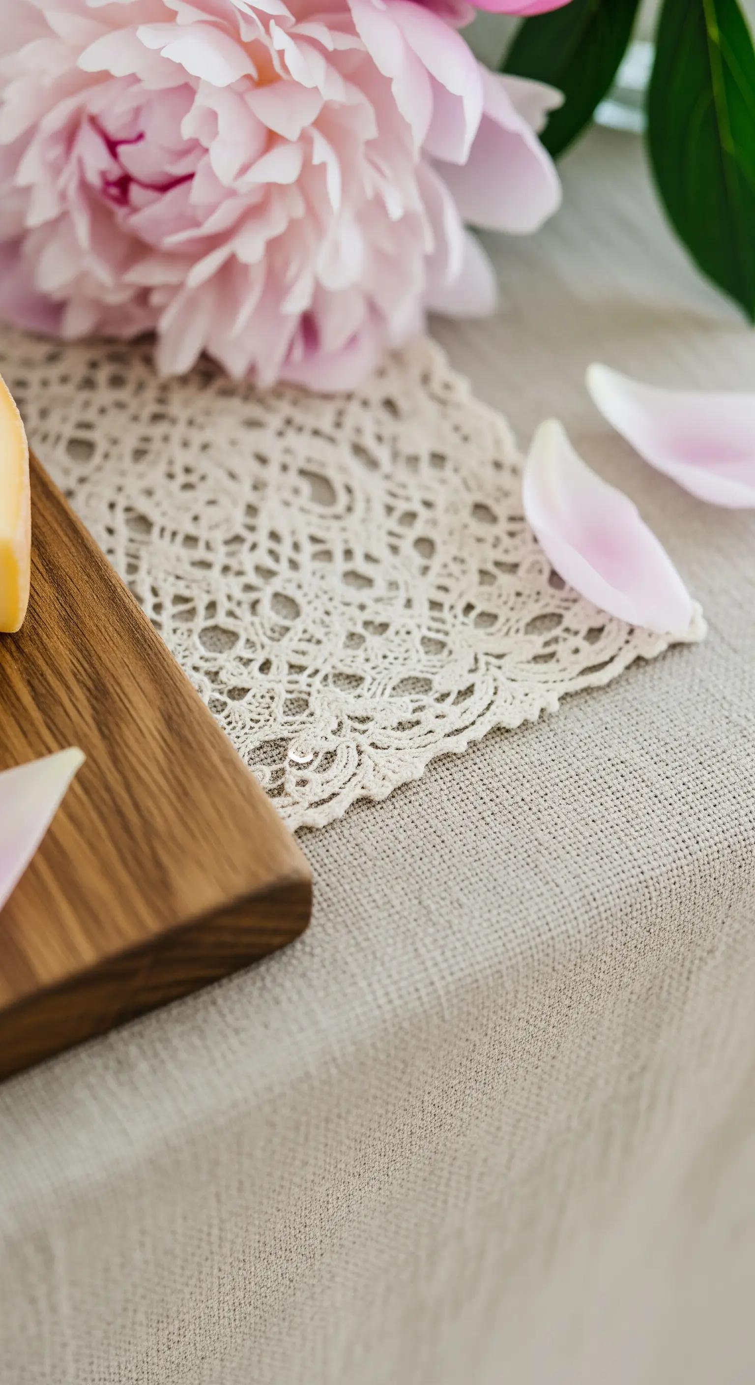 Dettaglio di una tovaglia in lino, centrino in pizzo e petali di peonia.