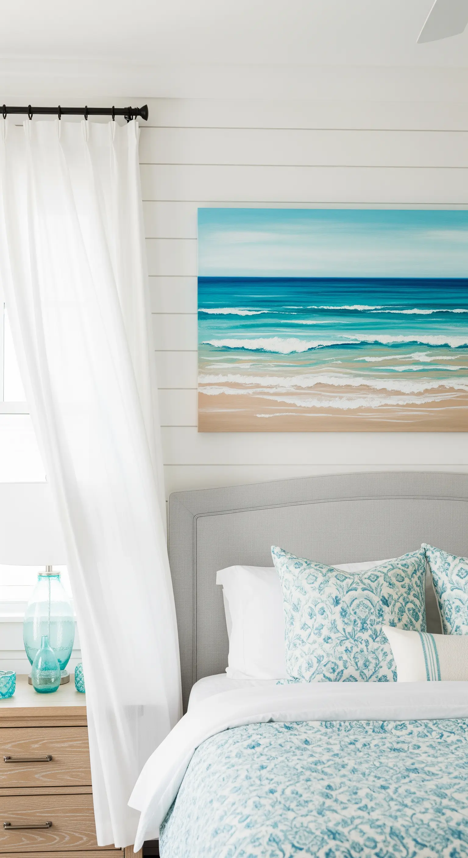 Quadro con paesaggio marino astratto sopra un letto con testiera grigia e cuscini a tema.