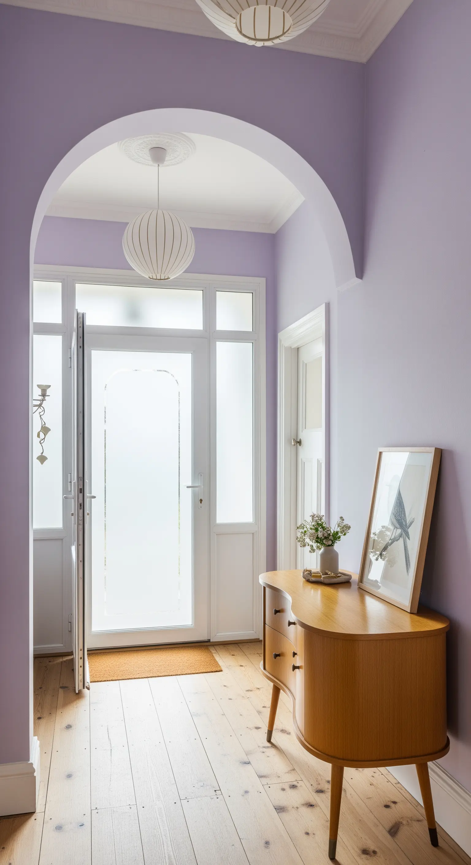 Ingresso color lilla con consolle in legno dalle forme arrotondate e porta a vetro.
