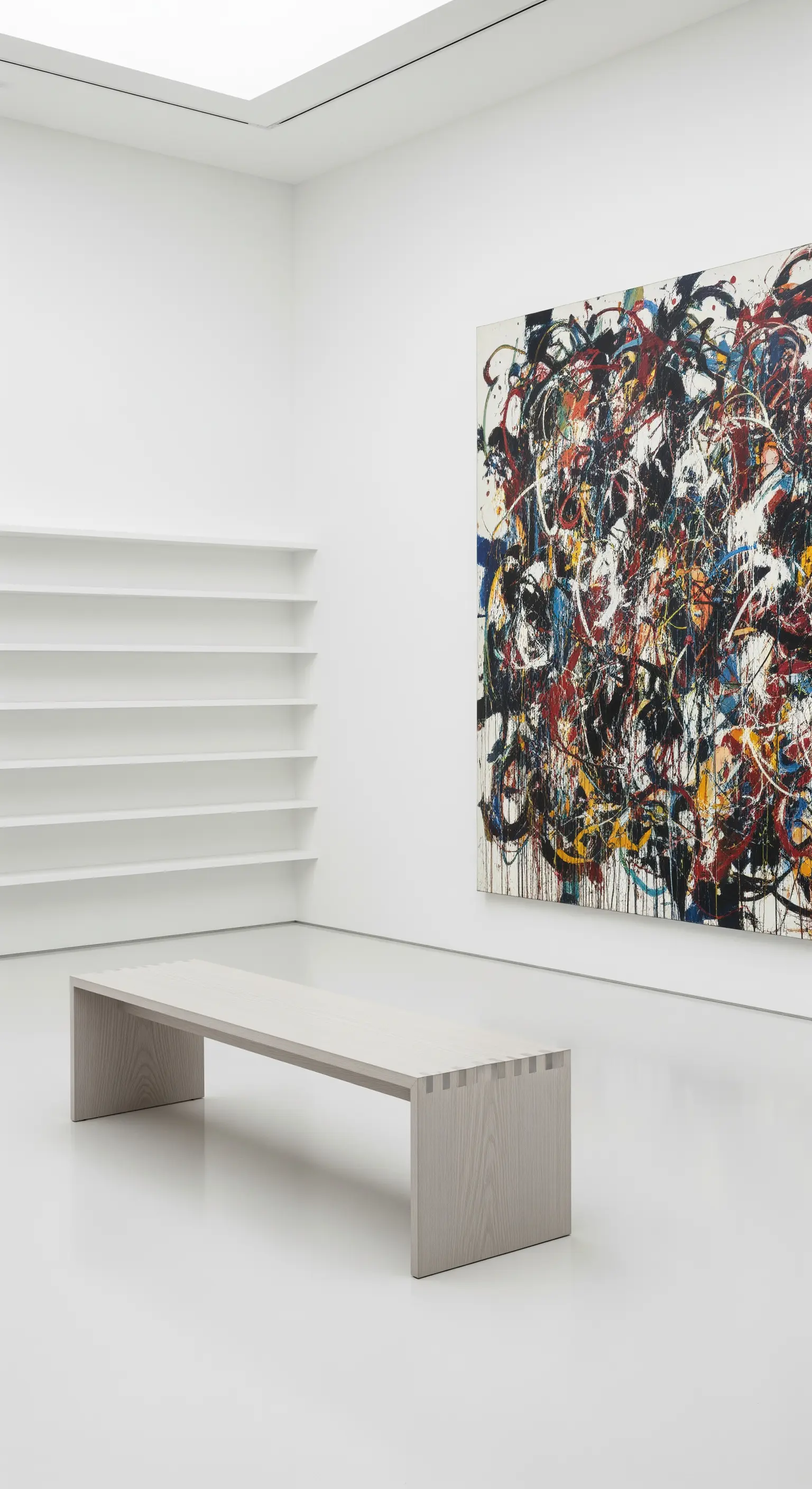 Spazio bianco da galleria d'arte con mensole basse e un enorme quadro astratto colorato.