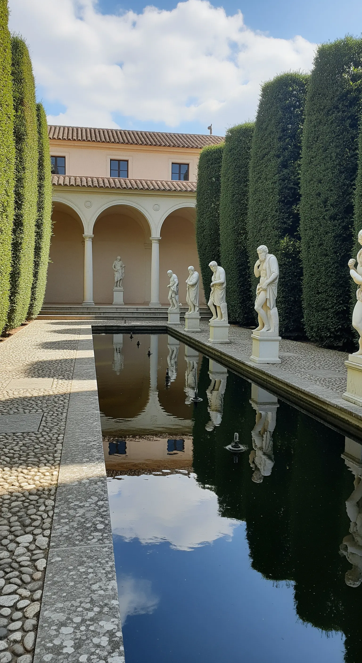 Cortile con lunga vasca d'acqua riflettente e una fila di statue classiche bianche.
