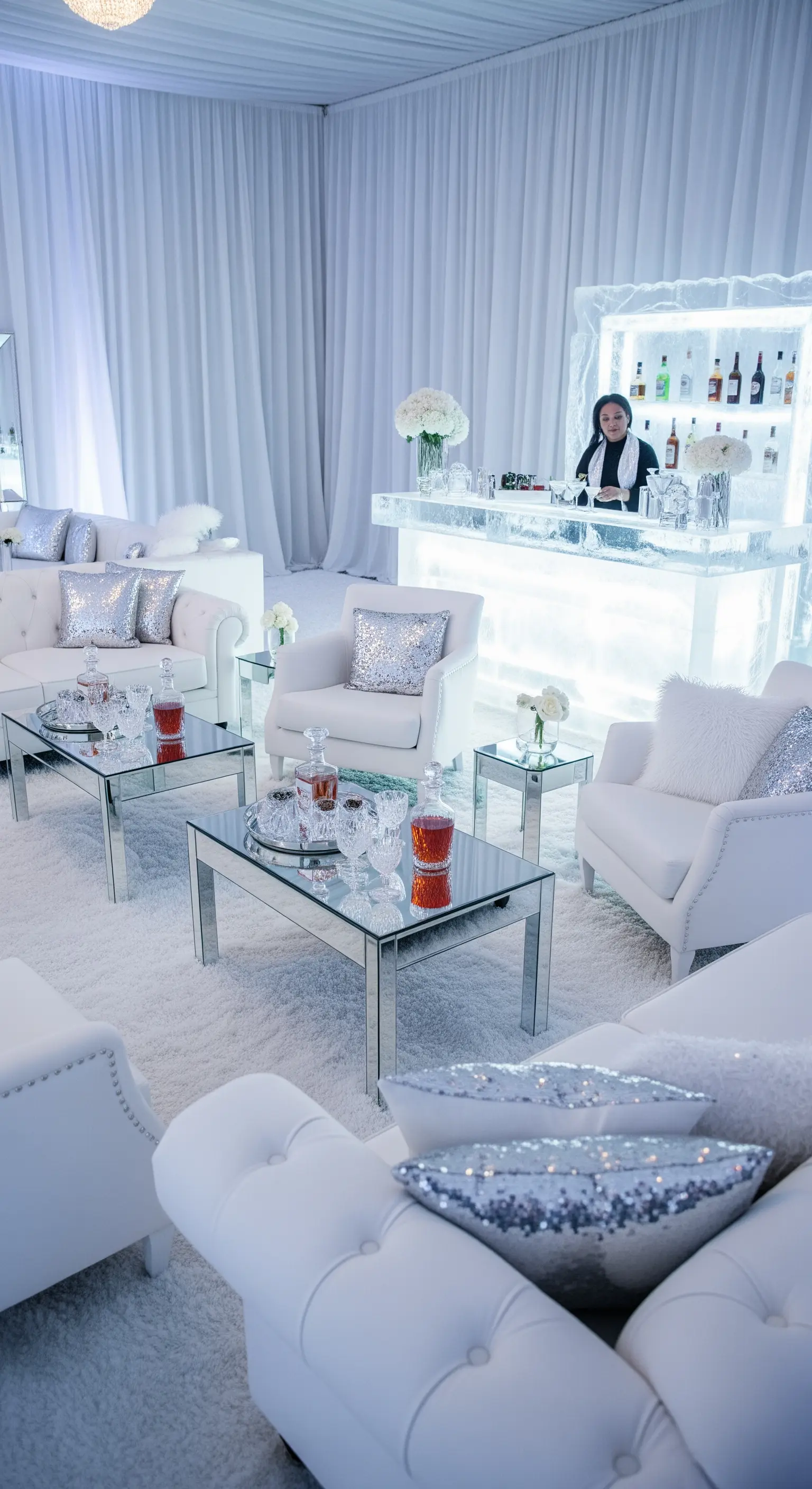 Area lounge bianca con cuscini argentati, tavoli a specchio e un ice bar.