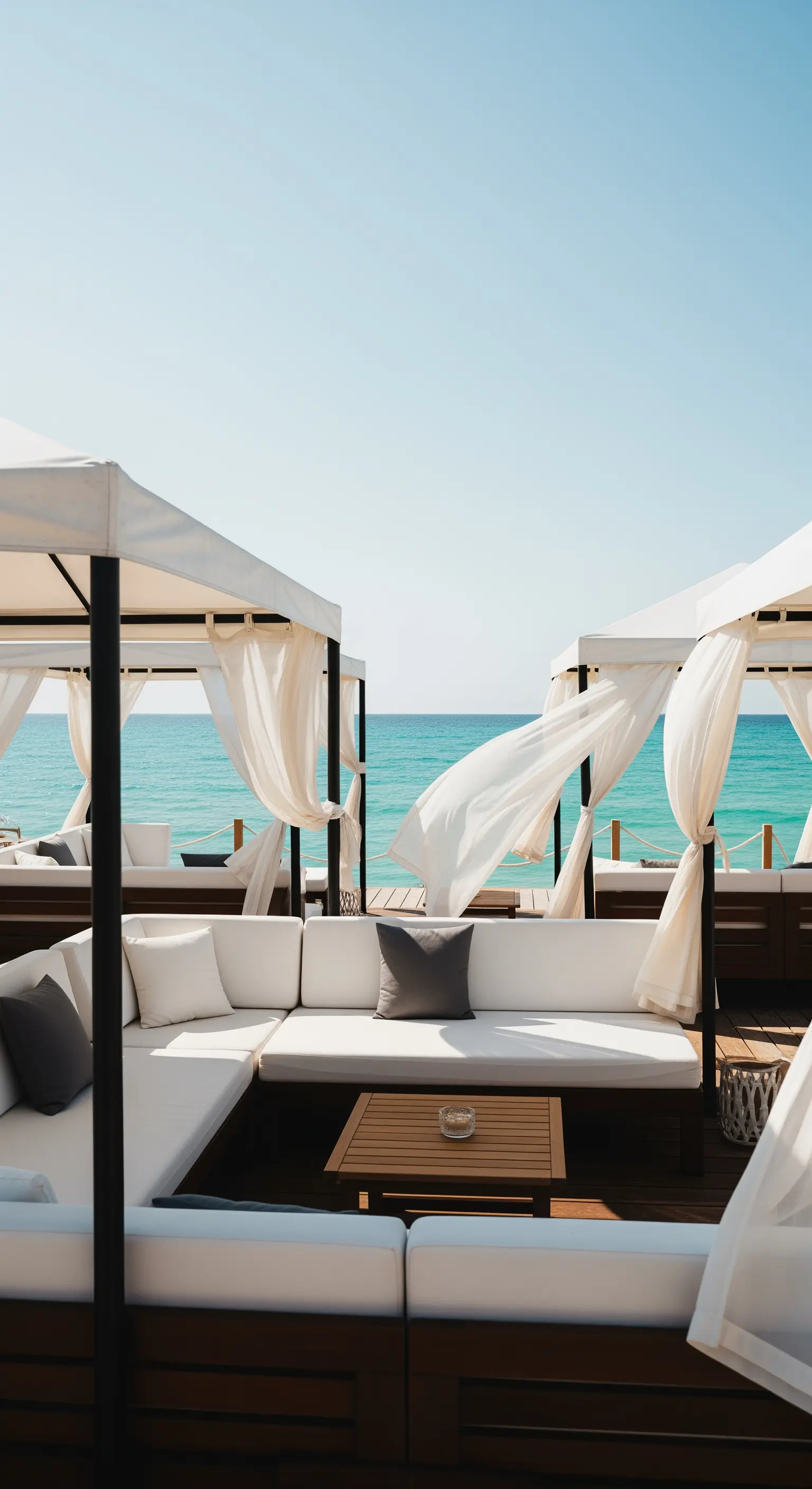 Area lounge sulla spiaggia con divani bianchi e gazebo con tende svolazzanti