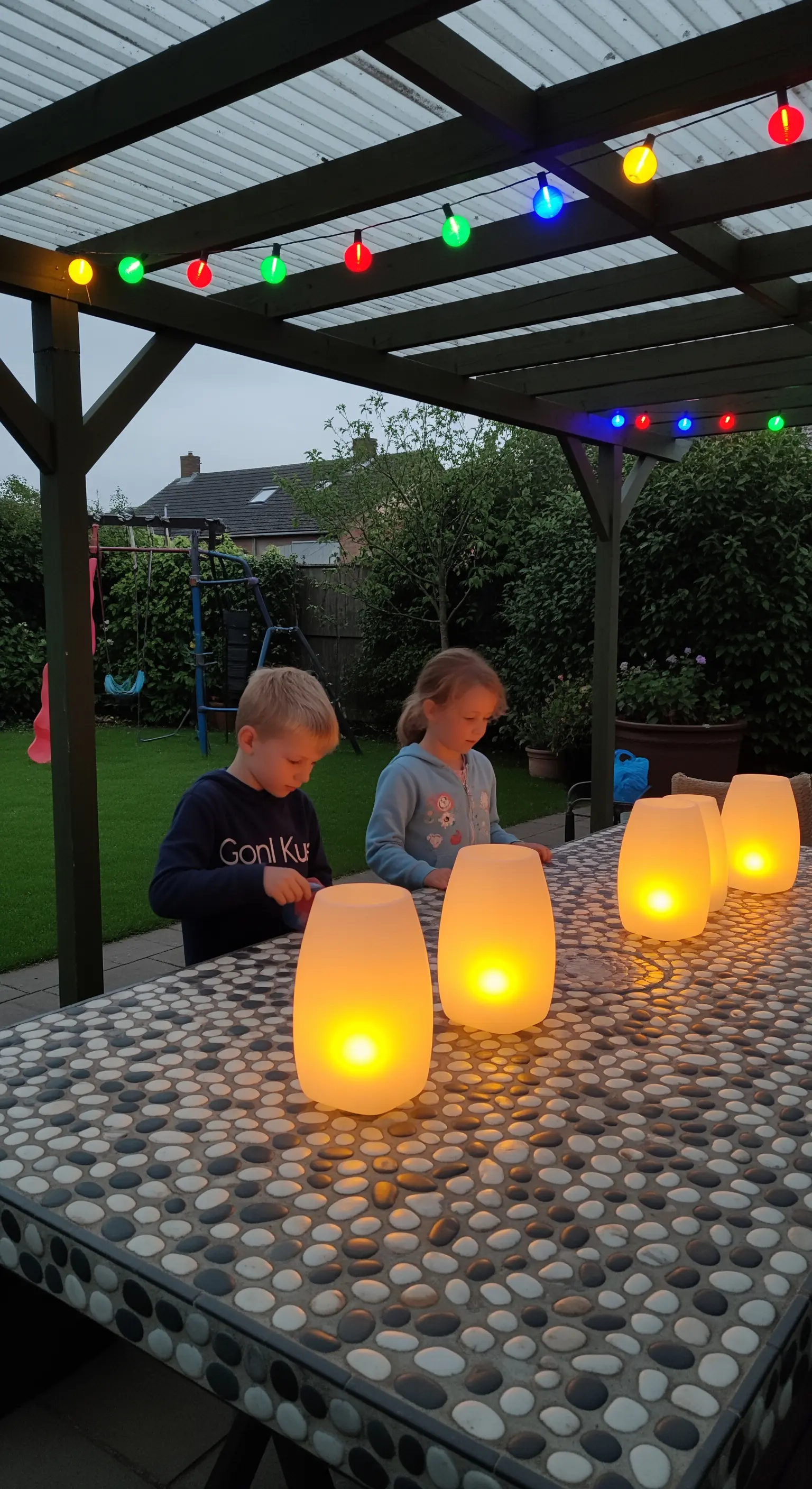 Bambini a un tavolo da esterno con mosaico di ciottoli, illuminato da lampade LED portatili