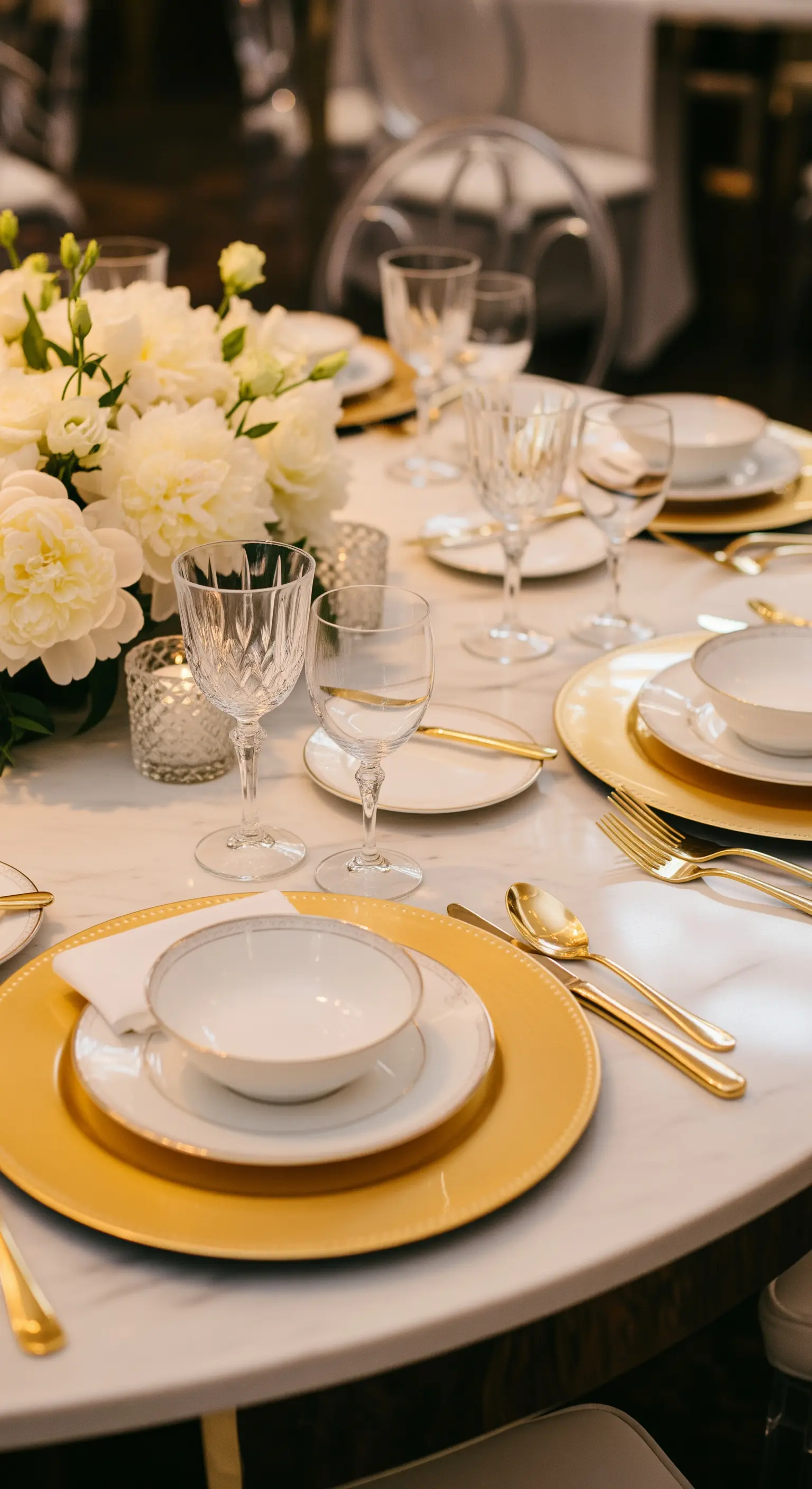 Tavola su piano in marmo con sottopiatti dorati e bicchieri di cristallo.