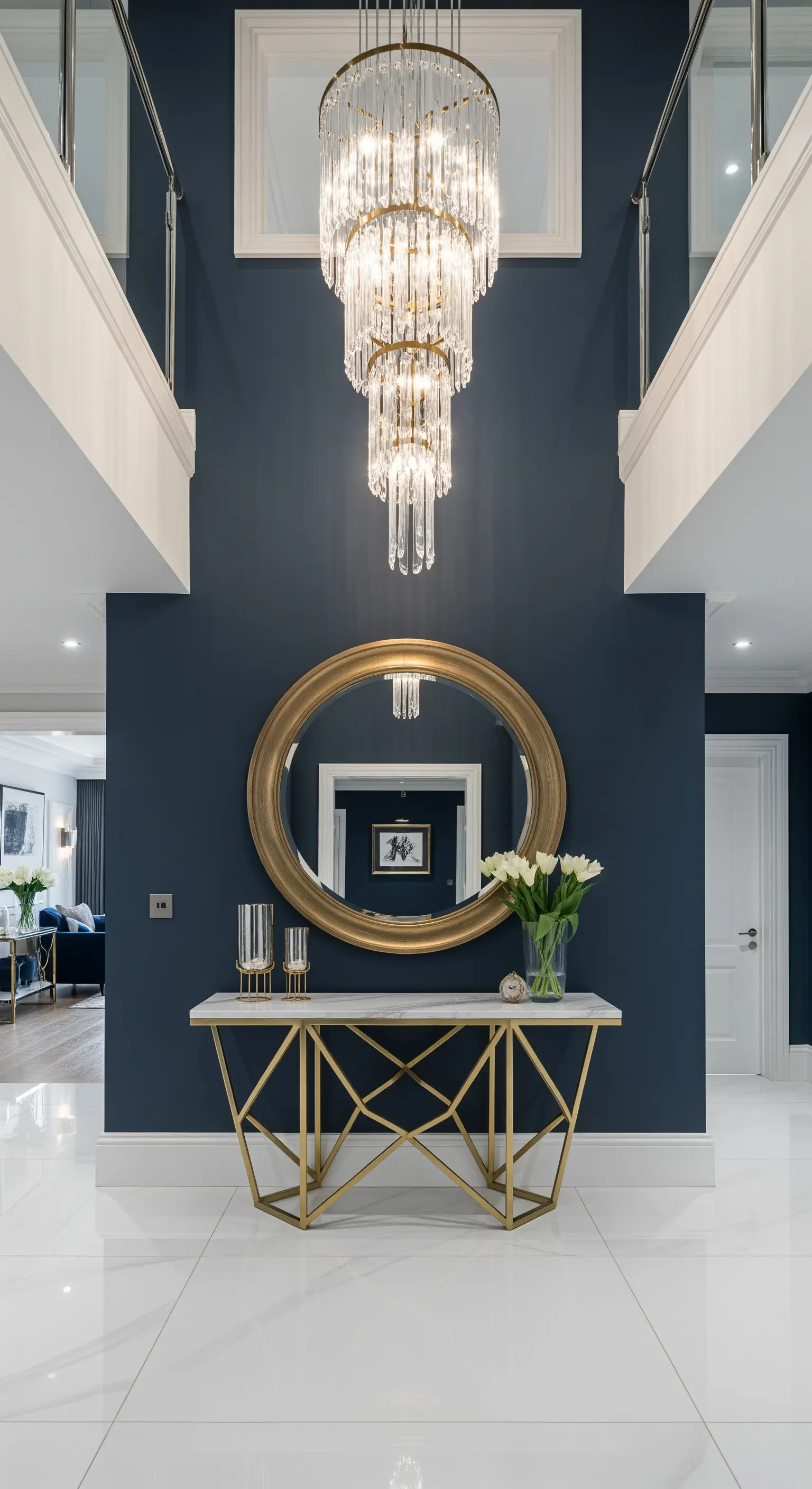 Consolle dorata e specchio rotondo su parete blu scuro, con grande lampadario in cristallo.