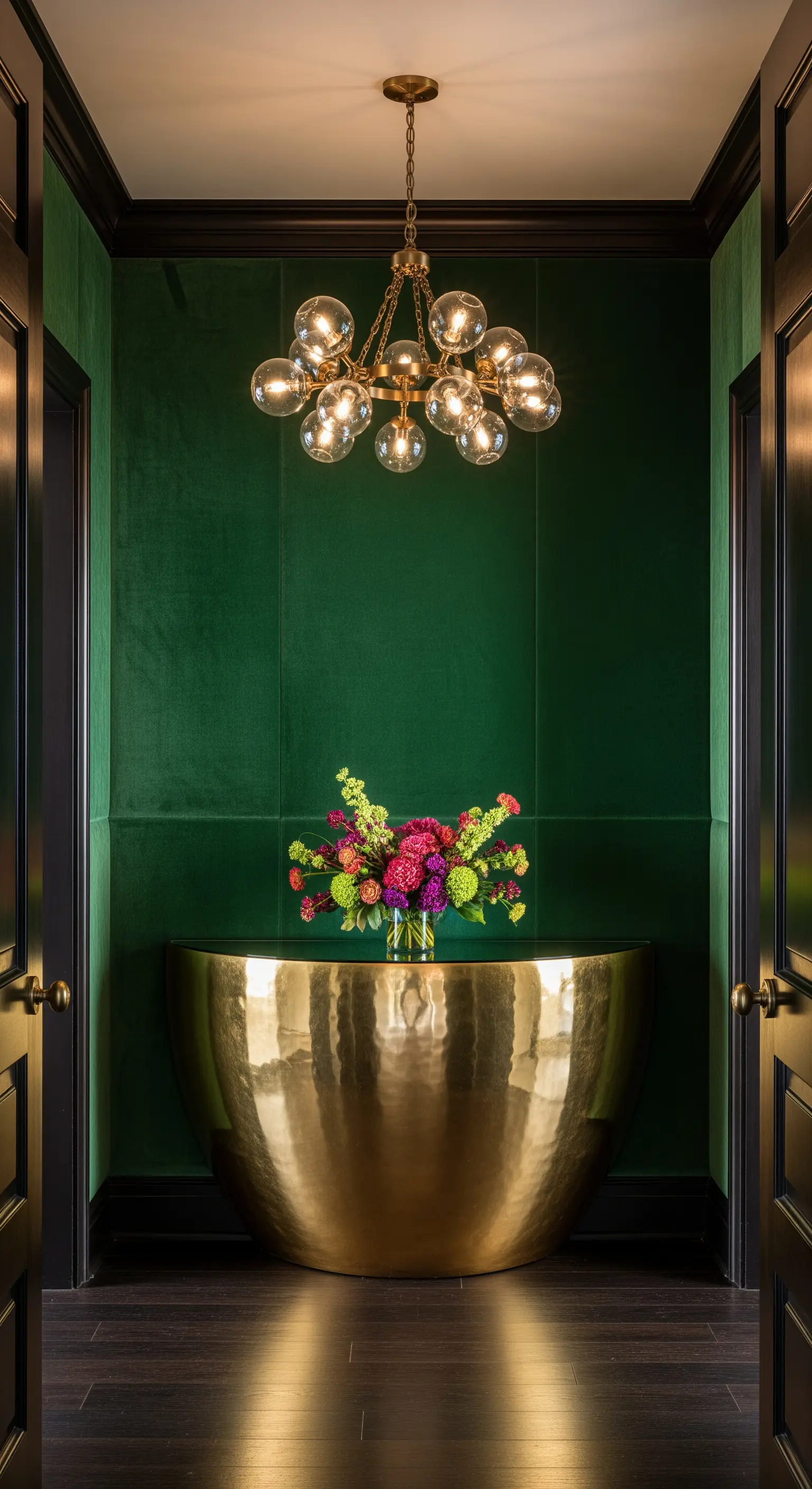 Ingresso con pareti in velluto verde, consolle in oro martellato e lampadario a bolle.