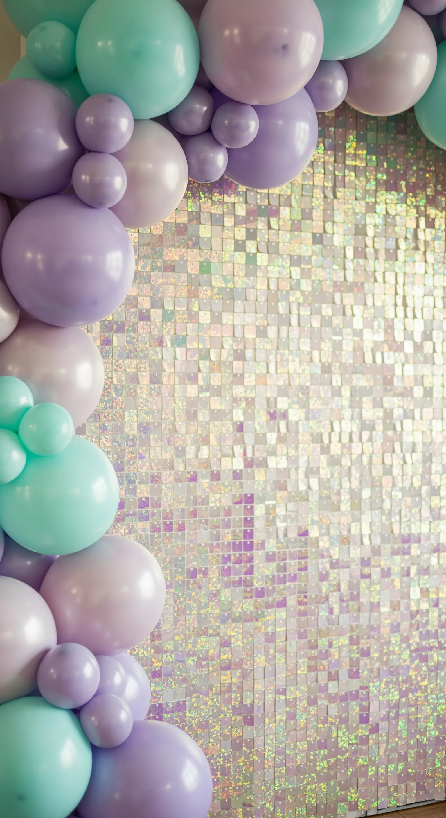 Backdrop di paillettes iridescenti con cornice di palloncini color pastello, lavanda e menta.