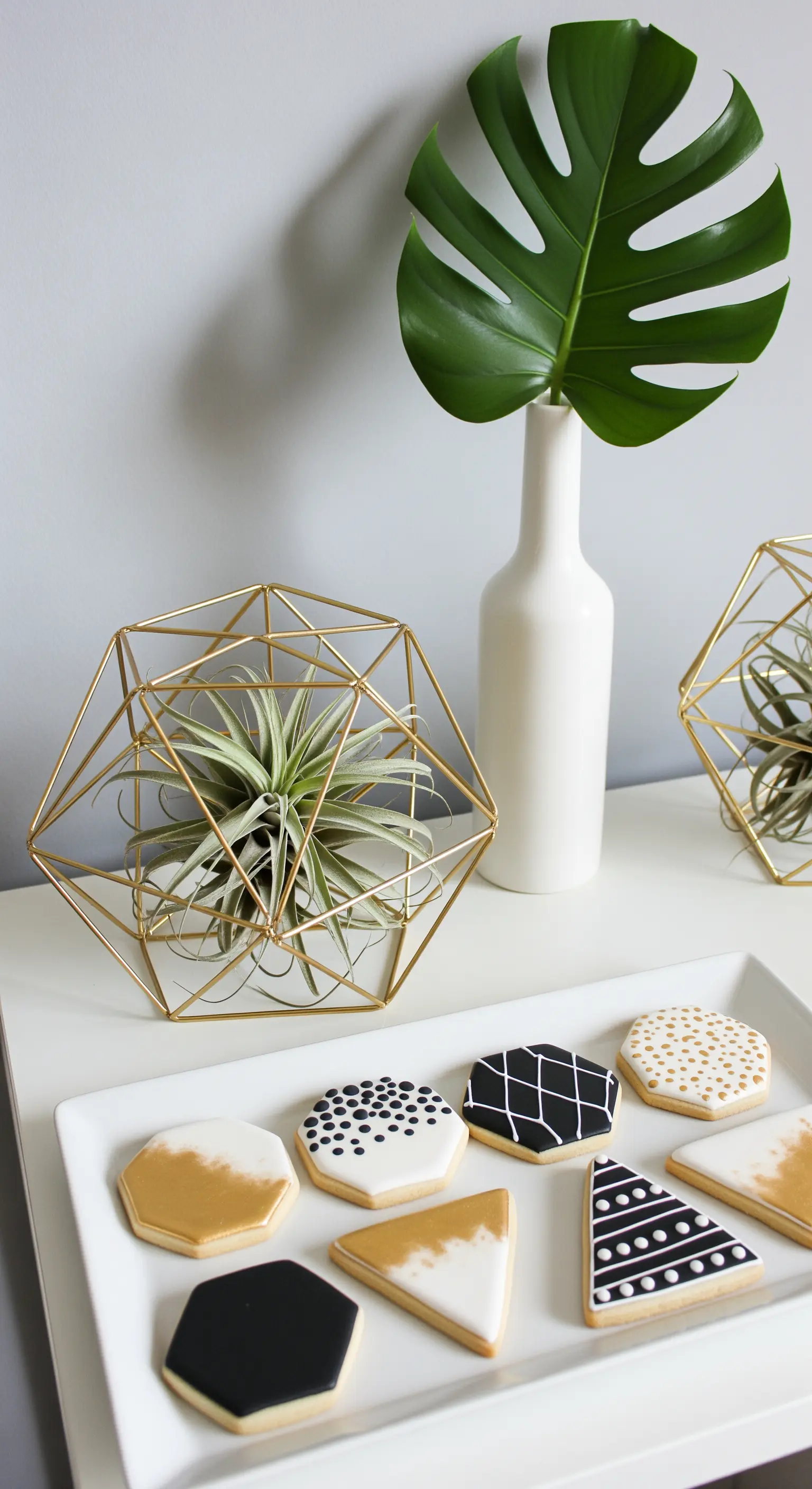 Biscotti decorati in bianco, nero e oro su un vassoio con decorazioni geometriche metalliche.