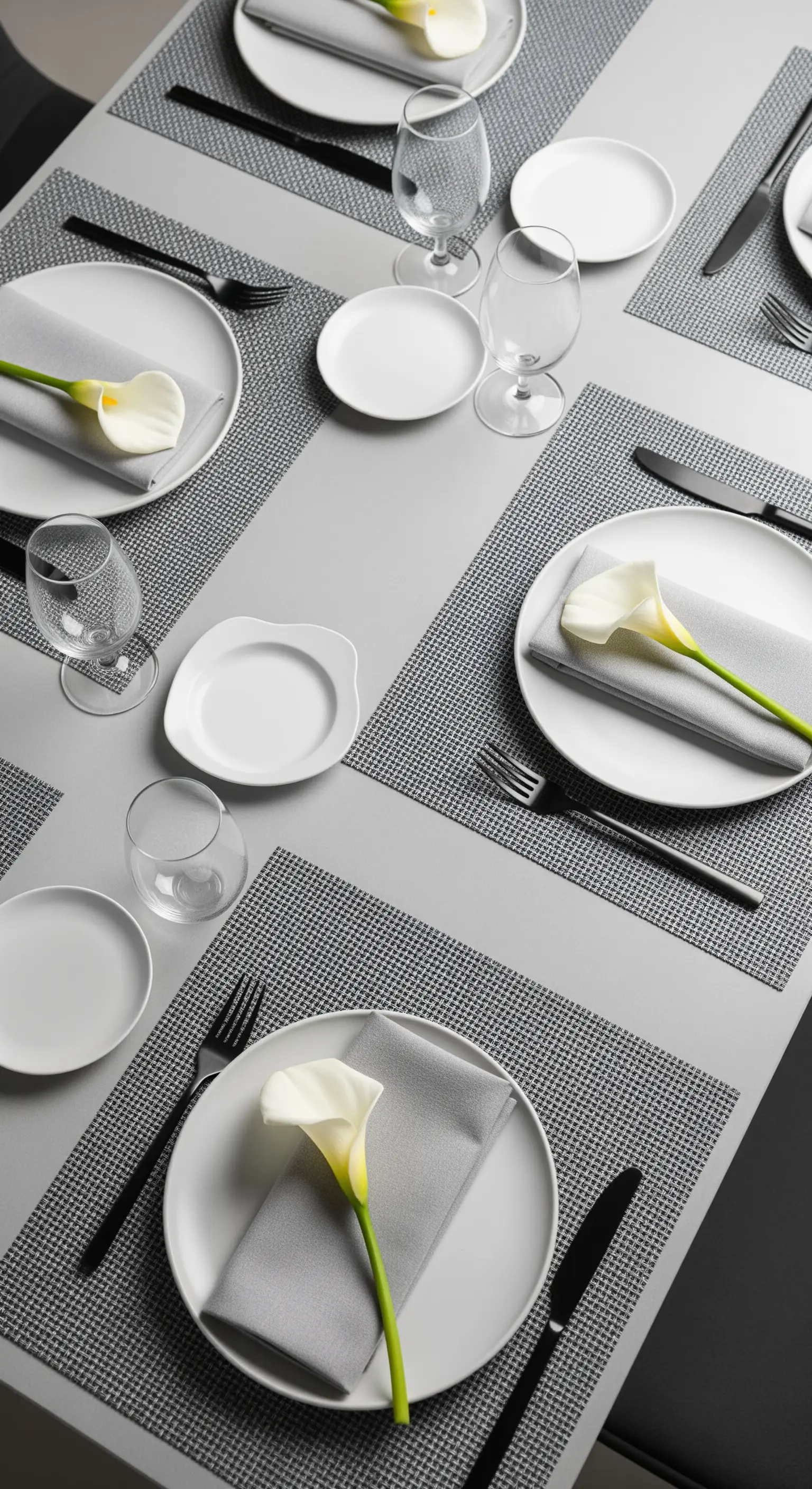 Tavola minimalista con piatti bianchi, posate nere e una calla su ogni posto.