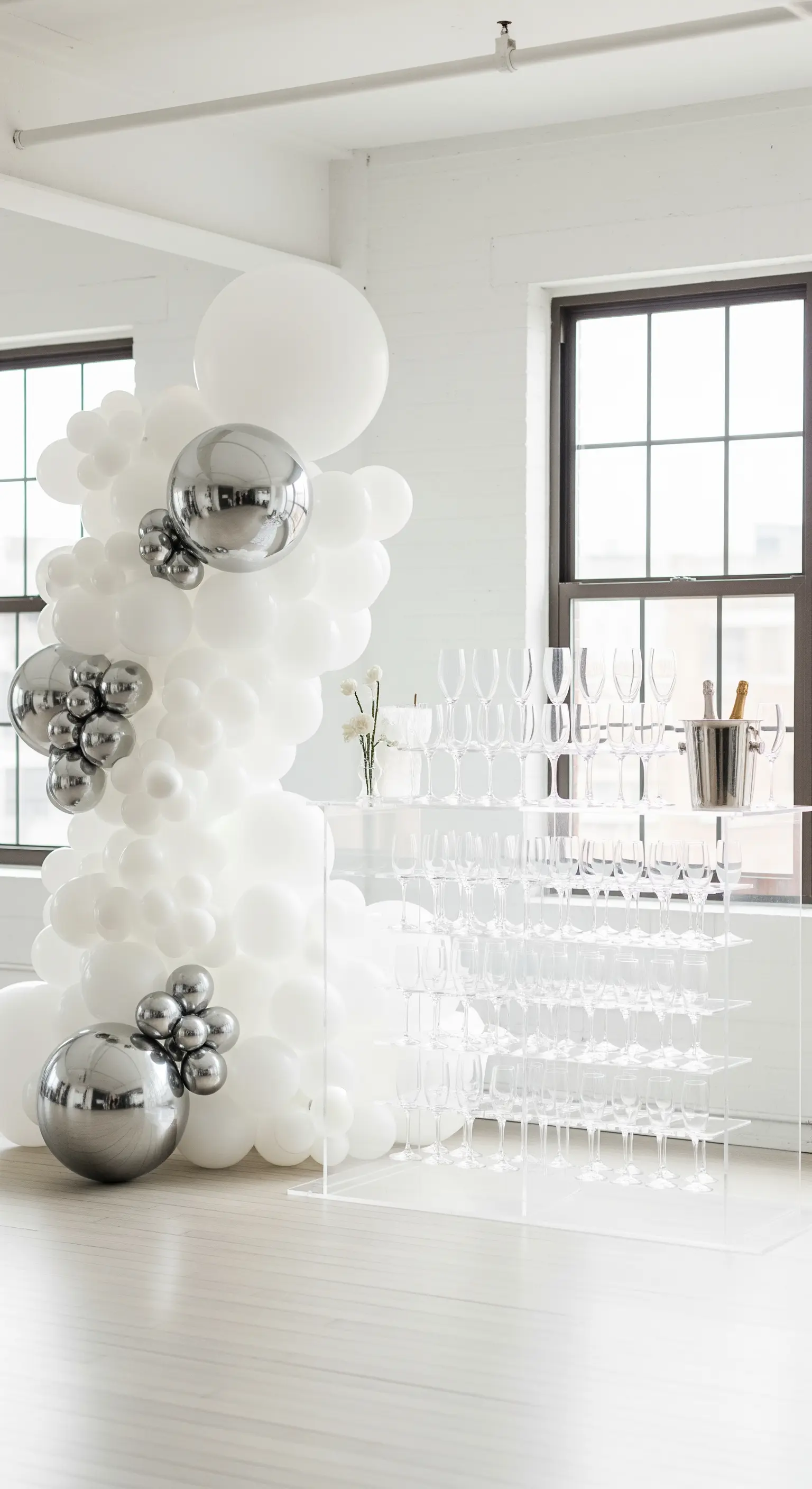 Allestimento minimalista con palloncini bianchi e sfere argento cromato in un loft luminoso.