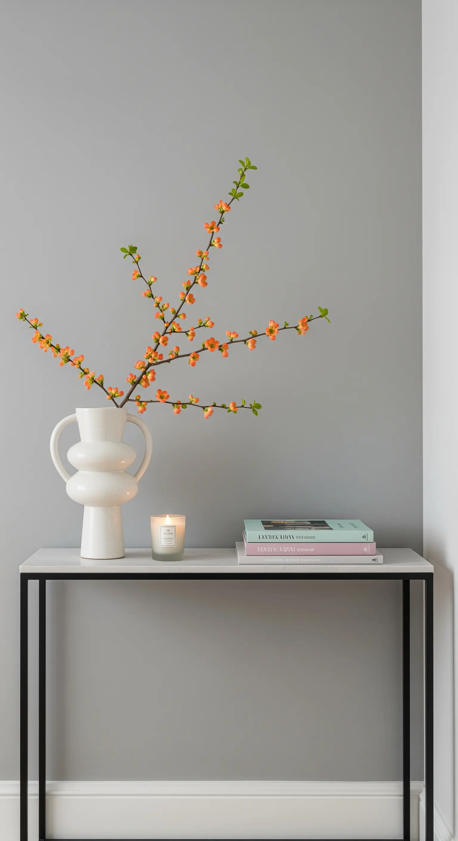 Consolle minimalista con un vaso bianco scultoreo contenente rami fioriti arancioni.