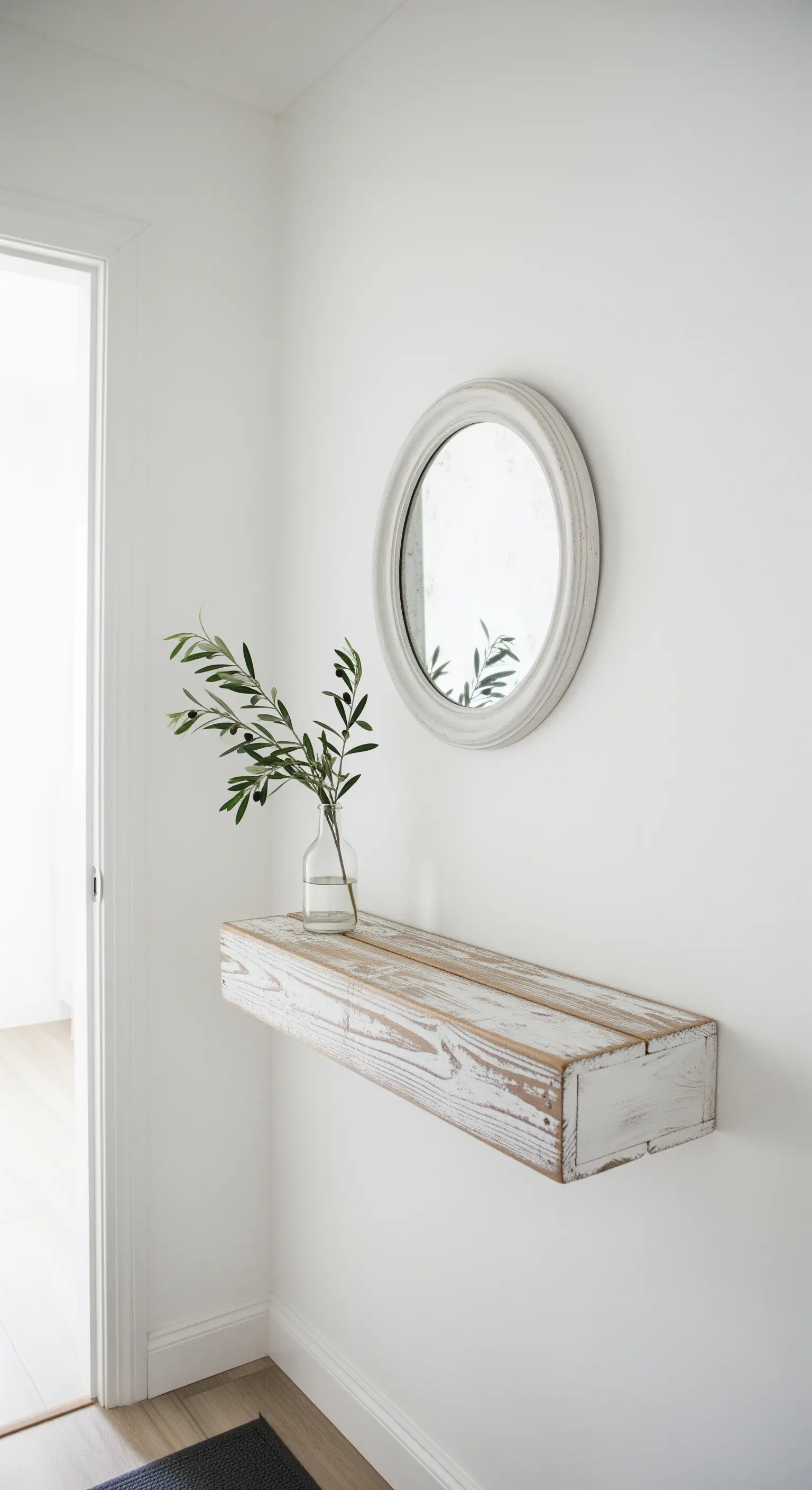 Mensola sospesa in legno sbiancato con un piccolo specchio rotondo appeso sopra.
