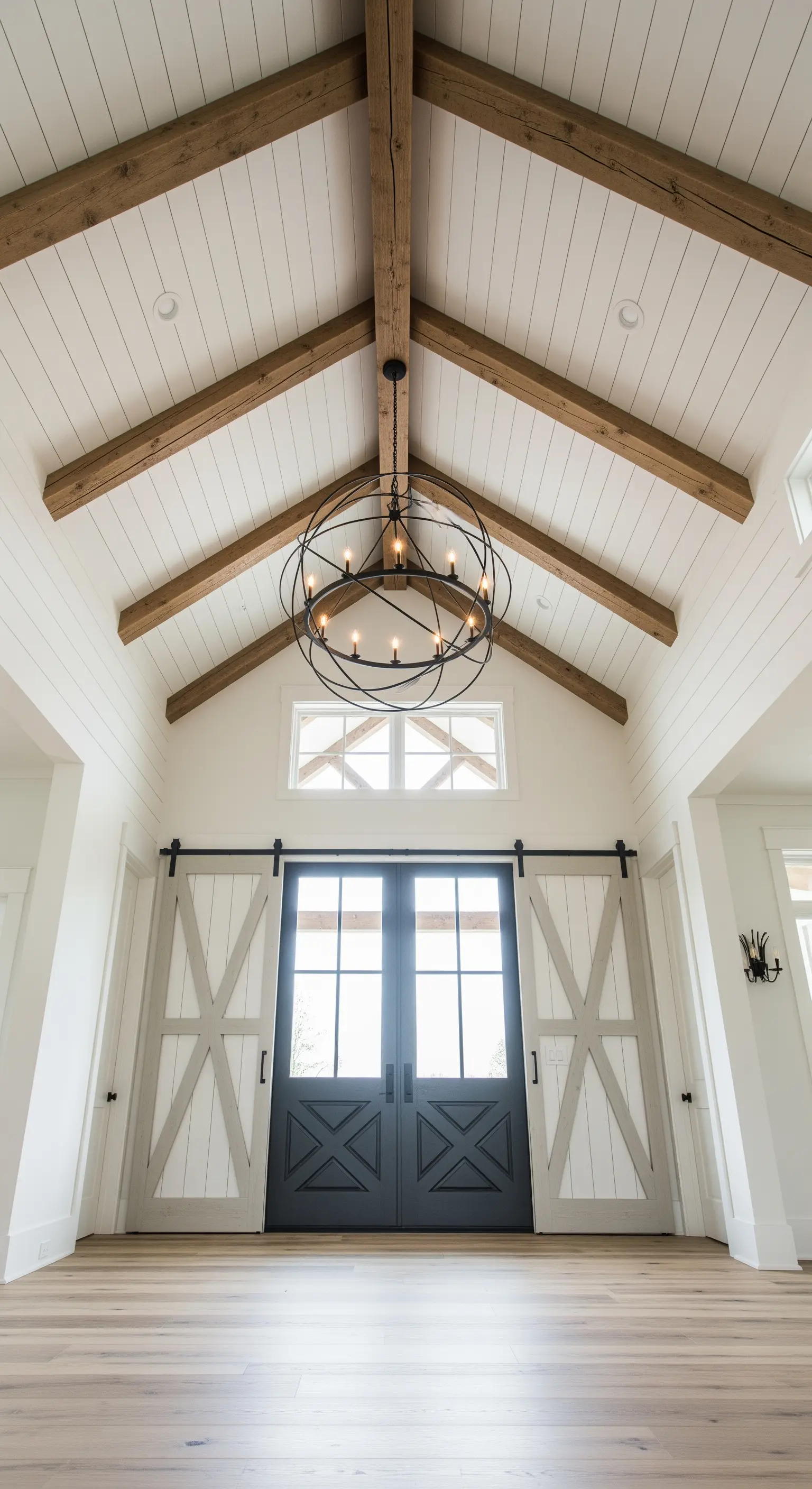 Ingresso in stile farmhouse con soffitto a capanna, travi in legno e porte nere a X.